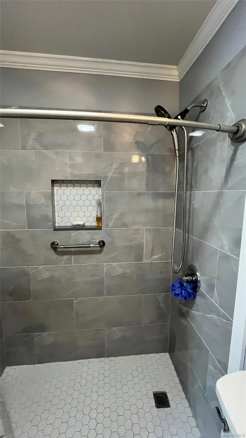 Shower enclosure featuring grey large-format tile walls, a white hexagonal mosaic tile floor, and a built-in shower niche with matching hexagonal tile Shower enclosure featuring grey large-format tile walls, a white hexagonal mosaic tile floor, and a built-in shower niche with matching hexagonal tile