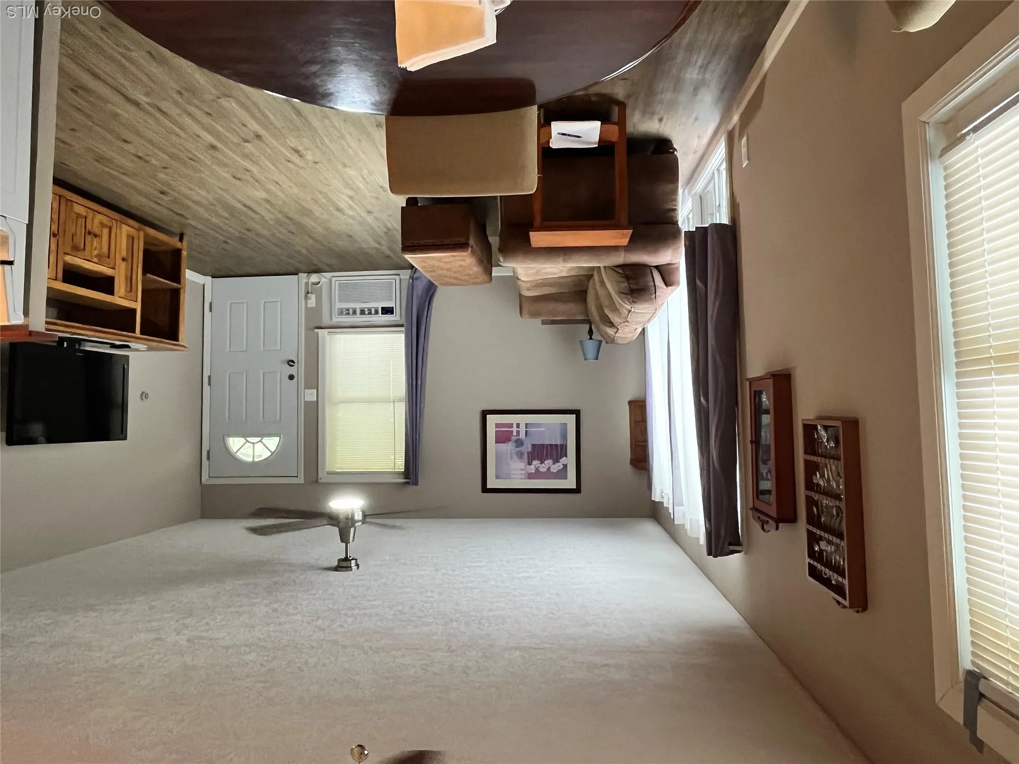 Open living area featuring wood-finish flooring, a white paneled entry door with an arched window insert, and a ceiling fan with integrated lighting Open living area featuring wood-finish flooring, a white paneled entry door with an arched window insert, and a ceiling fan with integrated lighting