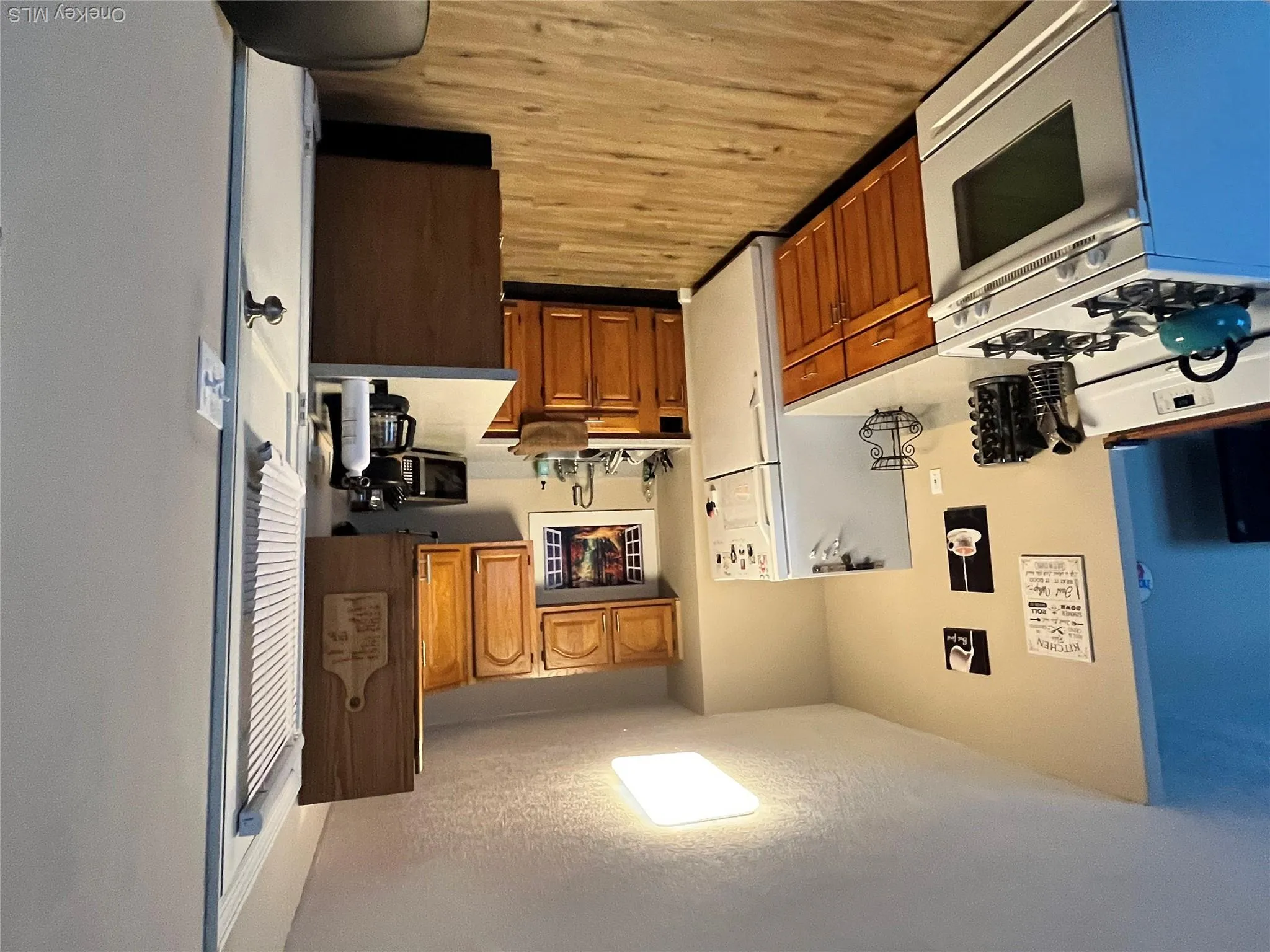 L-shaped kitchen featuring wood cabinetry, white appliances, and wood-finish flooring L-shaped kitchen featuring wood cabinetry, white appliances, and wood-finish flooring