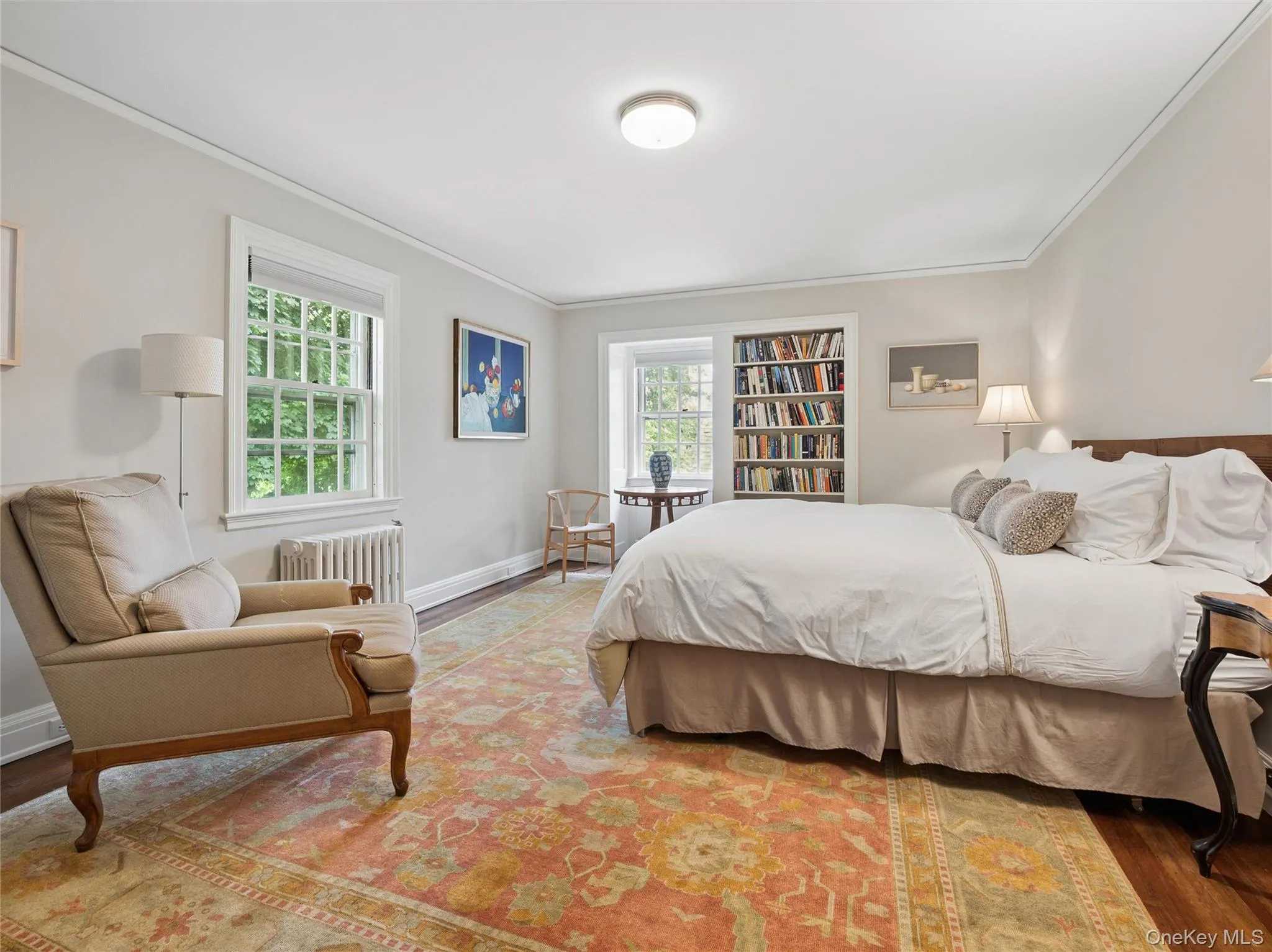Spacious guest room with ensuite bath room featuring rich wood flooring, built-in shelving, two large windows, crown molding, and a ceiling-mounted light fixture Spacious guest room with ensuite bath room featuring rich wood flooring, built-in shelving, two large windows, crown molding, and a ceiling-mounted light fixture