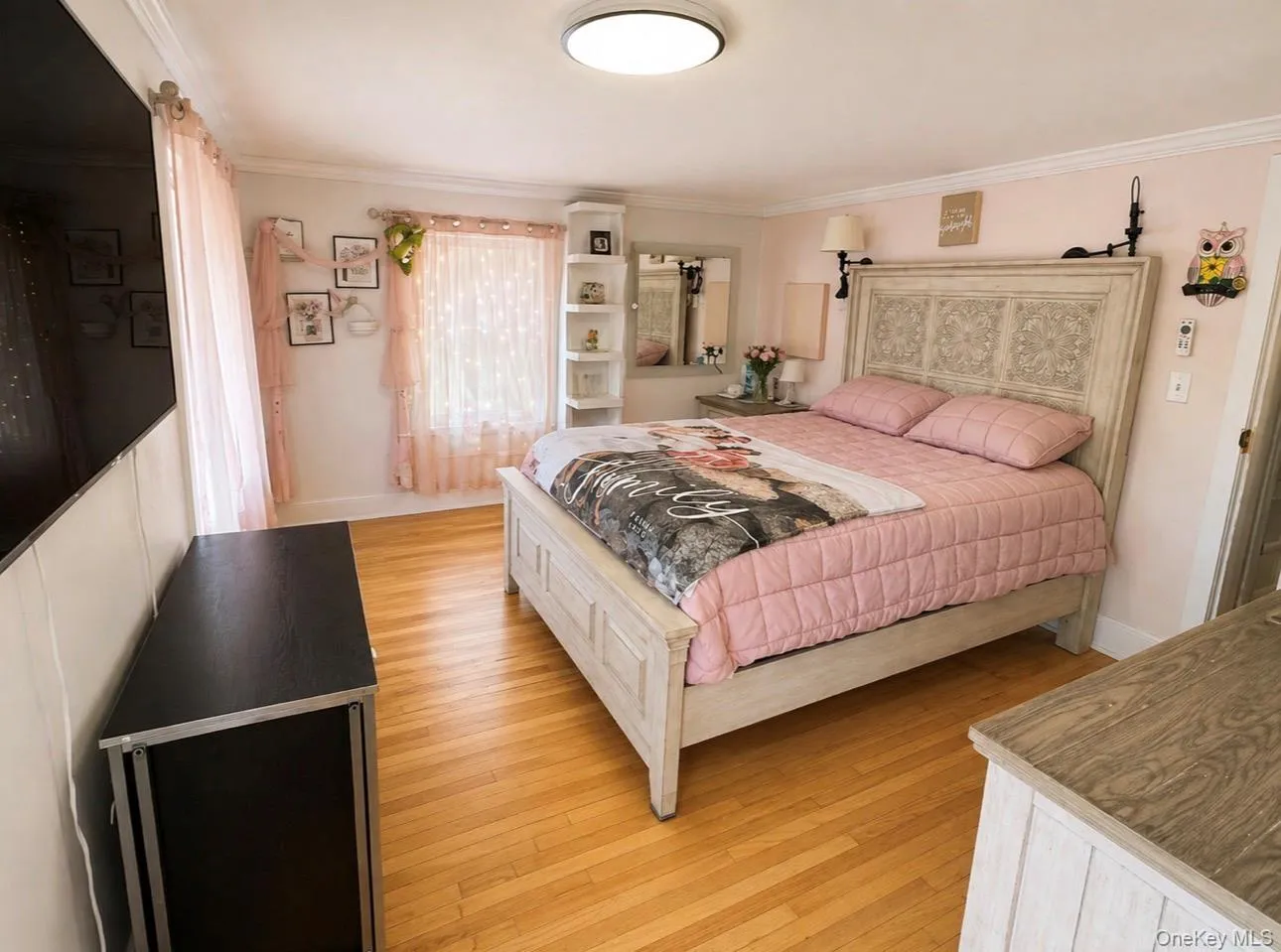 Bedroom featuring light wood-finish flooring, white crown molding, a built-in corner shelving unit, and wall-mounted sconce lighting Bedroom featuring light wood-finish flooring, white crown molding, a built-in corner shelving unit, and wall-mounted sconce lighting