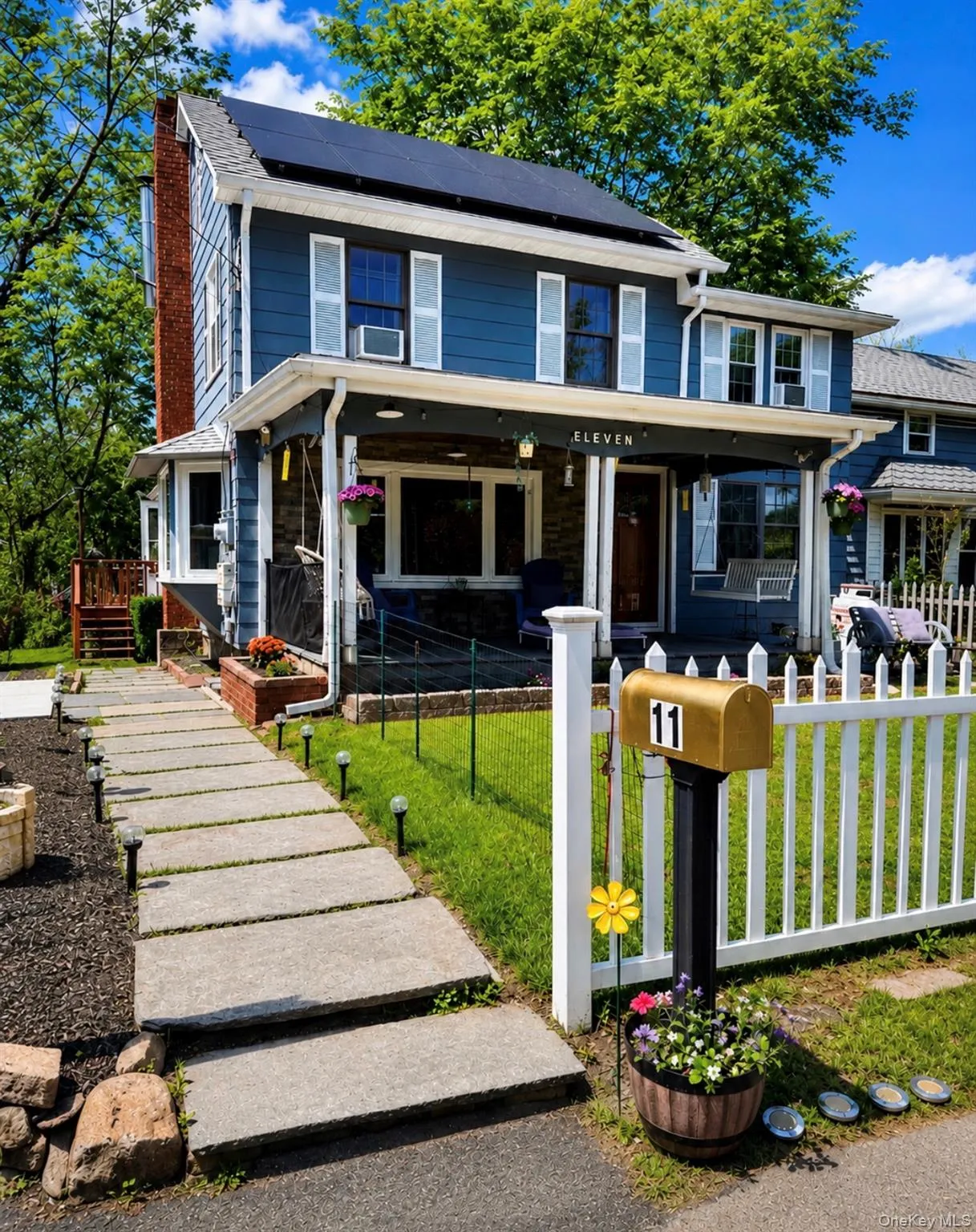 Two-story blue exterior featuring white window shutters, a covered front porch, and solar panels Two-story blue exterior featuring white window shutters, a covered front porch, and solar panels
