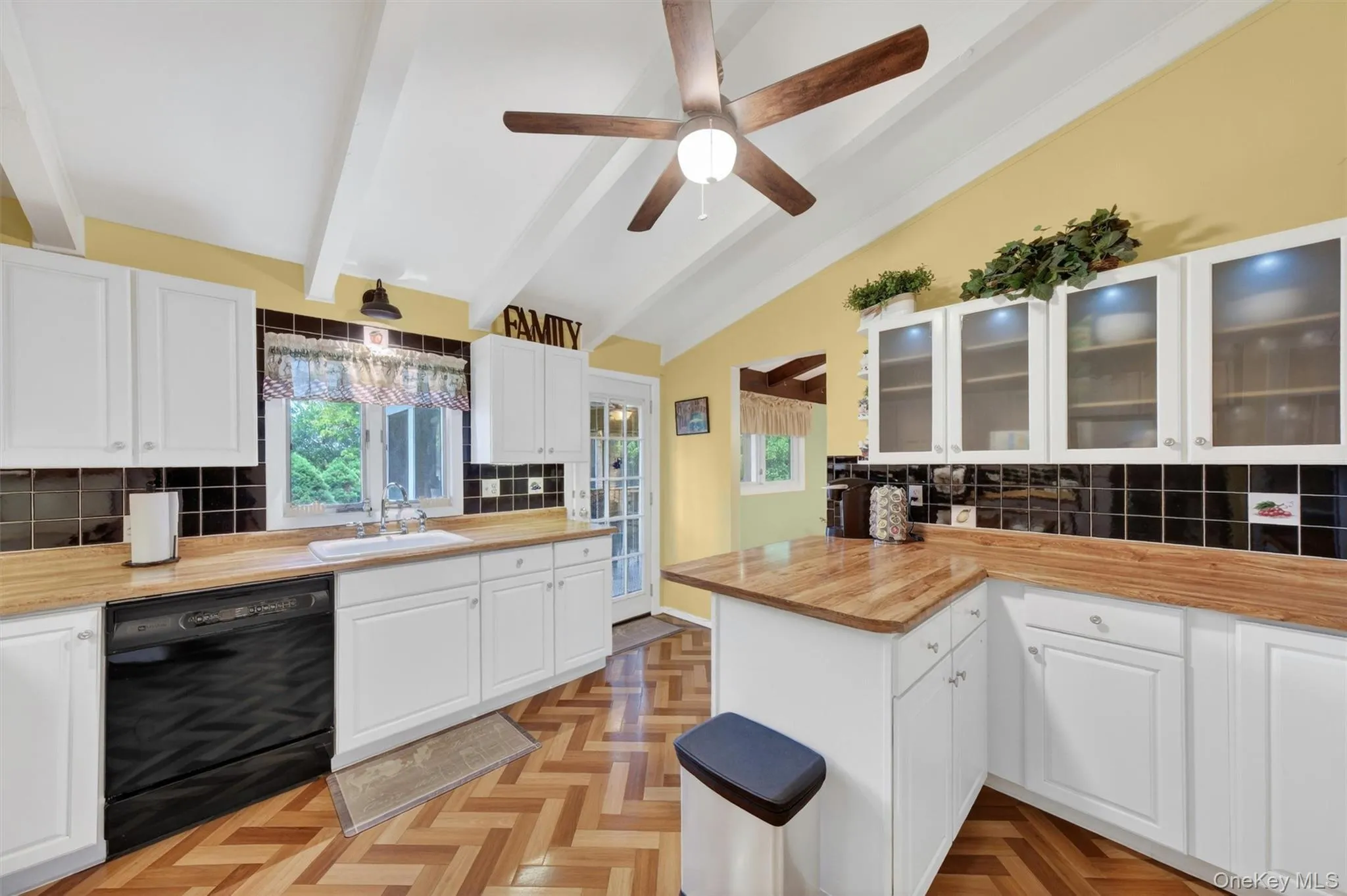 Kitchen featuring vaulted ceilings with exposed beams, wood-finish flooring in a herringbone pattern, white cabinetry, breakfast bar, tile backsplash, cabinet lighting and light wood-finish countertops Kitchen featuring vaulted ceilings with exposed beams, wood-finish flooring in a herringbone pattern, white cabinetry, breakfast bar, tile backsplash, cabinet lighting and light wood-finish countertops