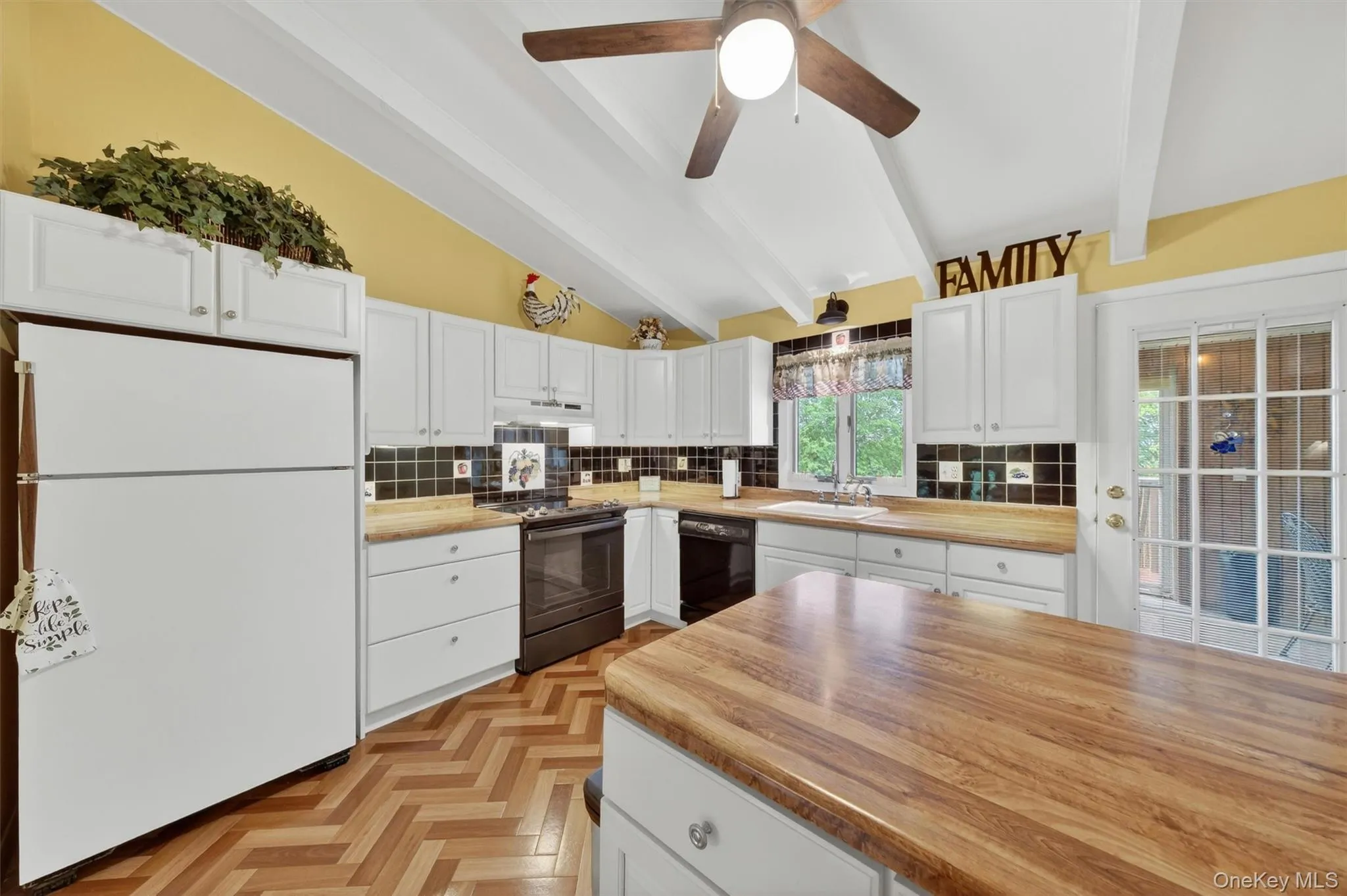 Kitchen featuring vaulted ceilings with exposed beams, wood-finish flooring in a herringbone pattern, white cabinetry, breakfast bar, tile backsplash, cabinet lighting and light wood-finish countertops Kitchen featuring vaulted ceilings with exposed beams, wood-finish flooring in a herringbone pattern, white cabinetry, breakfast bar, tile backsplash, cabinet lighting and light wood-finish countertops