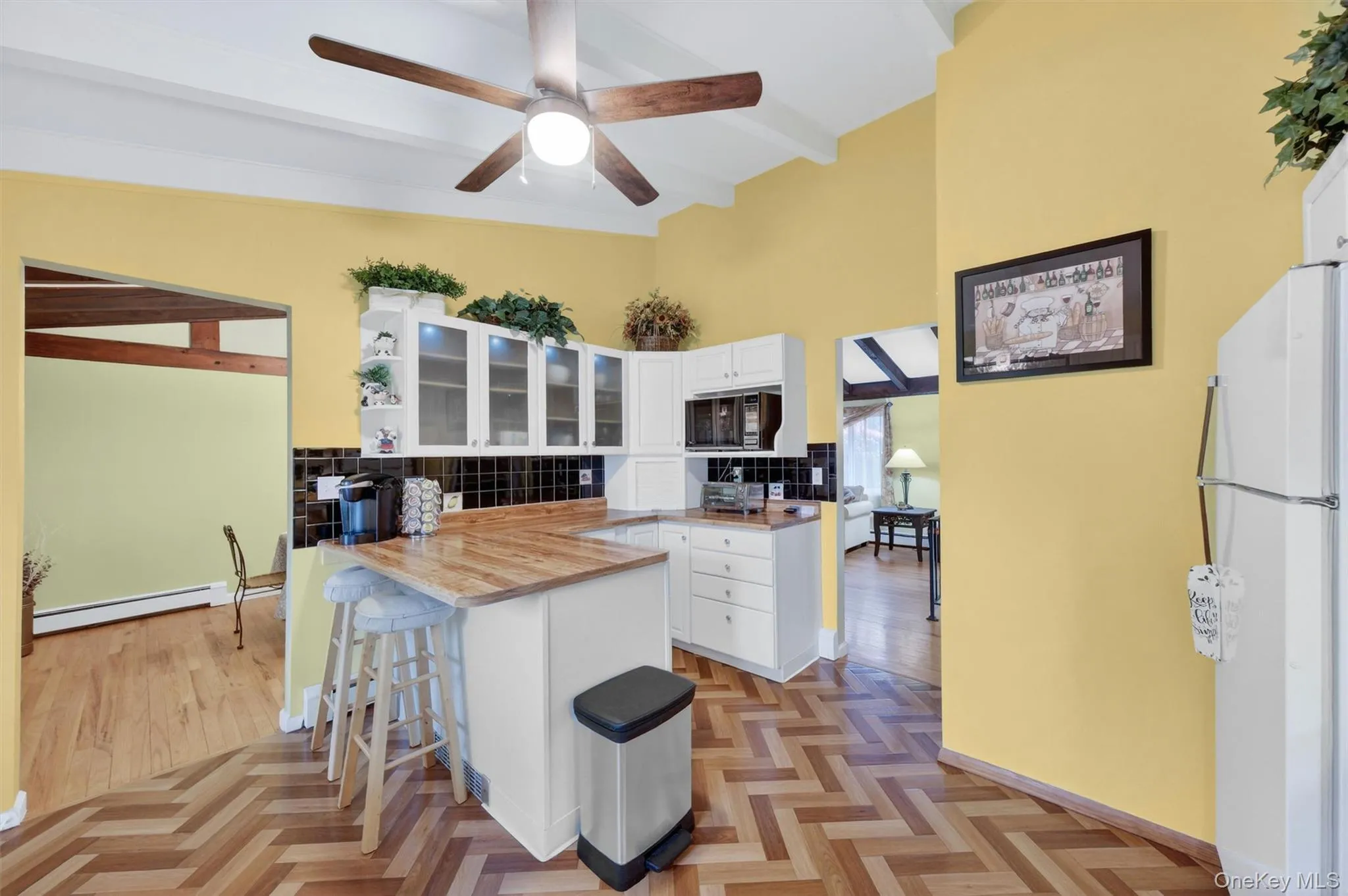 Kitchen featuring vaulted ceilings with exposed beams, wood-finish flooring in a herringbone pattern, white cabinetry, breakfast bar, tile backsplash, cabinet lighting and light wood-finish countertops Kitchen featuring vaulted ceilings with exposed beams, wood-finish flooring in a herringbone pattern, white cabinetry, breakfast bar, tile backsplash, cabinet lighting and light wood-finish countertops