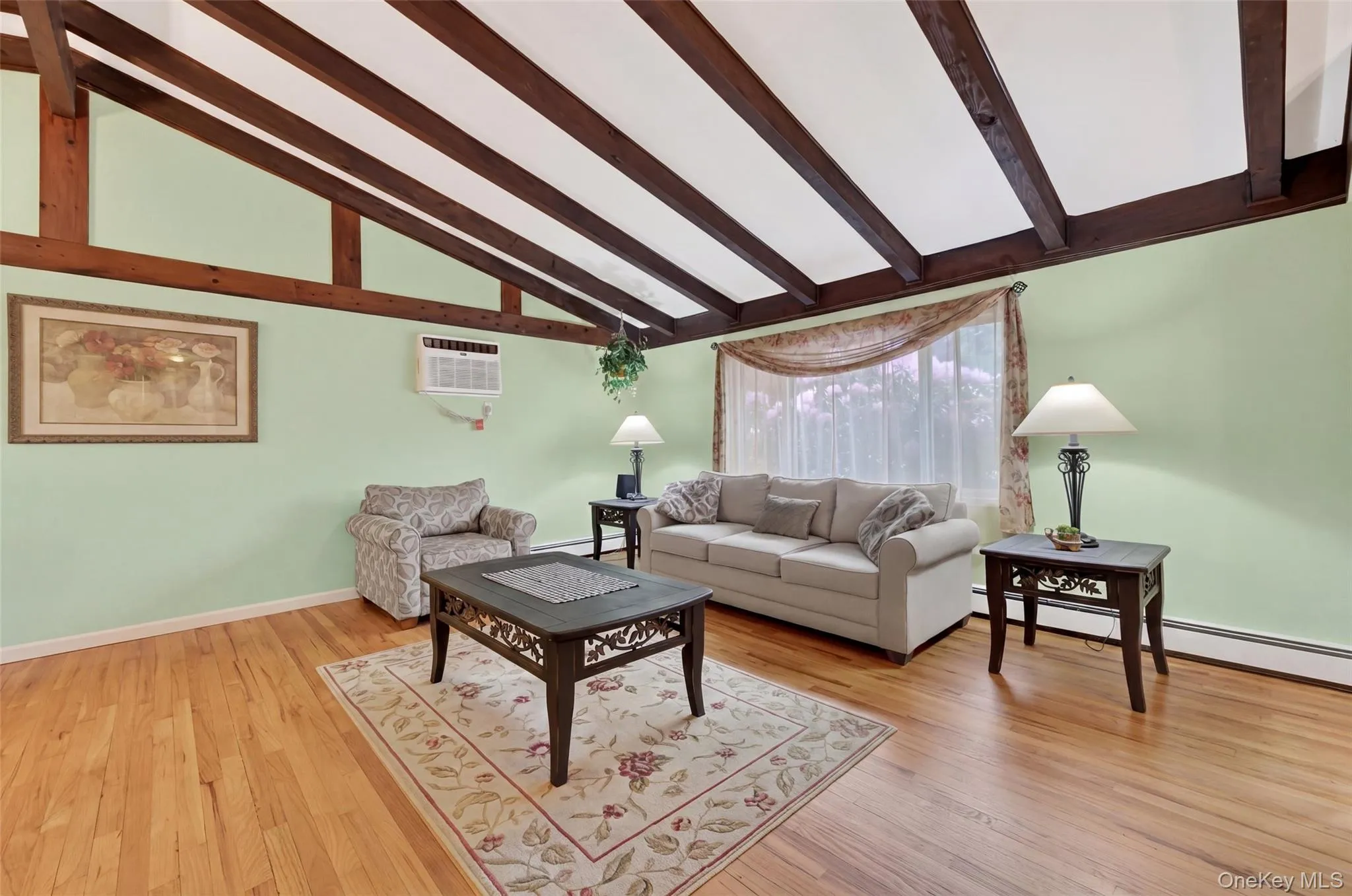 Living room with Vaulted ceilings with exposed wood beams, hardwood flooring, and a large window Living room with Vaulted ceilings with exposed wood beams, hardwood flooring, and a large window