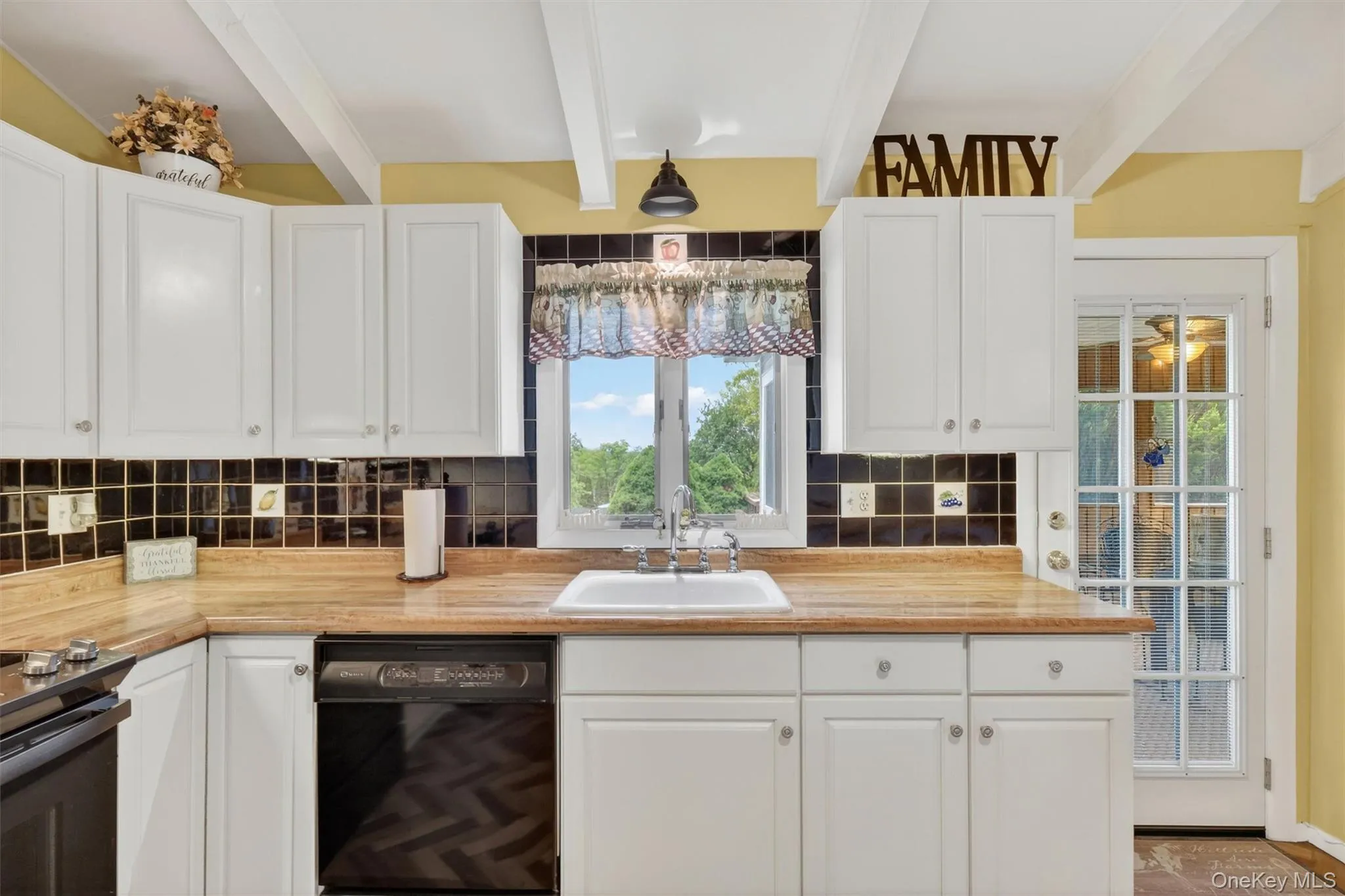 Kitchen featuring vaulted ceilings with exposed beams, wood-finish flooring in a herringbone pattern, white cabinetry, breakfast bar, tile backsplash, cabinet lighting and light wood-finish countertops Kitchen featuring vaulted ceilings with exposed beams, wood-finish flooring in a herringbone pattern, white cabinetry, breakfast bar, tile backsplash, cabinet lighting and light wood-finish countertops