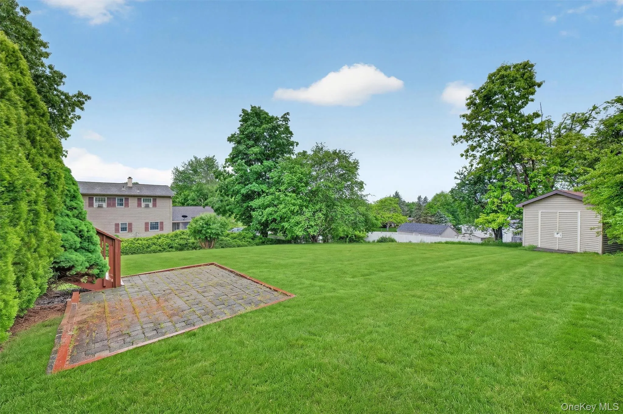 Expansive rear lawn with a paver patio and a utility shed Expansive rear lawn with a paver patio and a utility shed