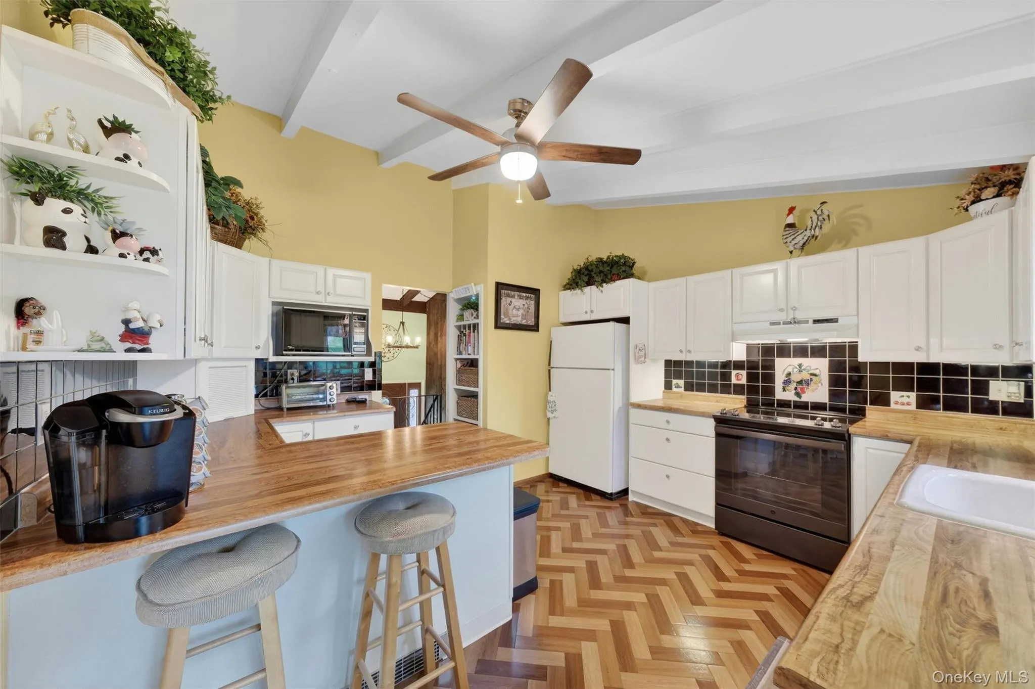 Kitchen featuring vaulted ceilings with exposed beams, wood-finish flooring in a herringbone pattern, white cabinetry, breakfast bar, tile backsplash, cabinet lighting and light wood-finish countertops Kitchen featuring vaulted ceilings with exposed beams, wood-finish flooring in a herringbone pattern, white cabinetry, breakfast bar, tile backsplash, cabinet lighting and light wood-finish countertops