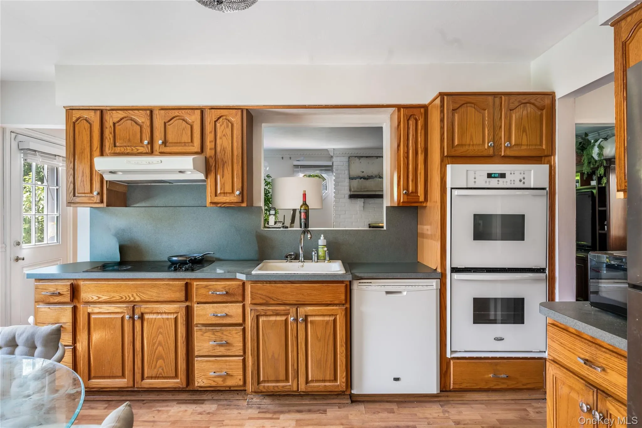 Kitchen featuring wood cabinetry, stone-finish countertops, built-in double ovens, and a pass-through window Kitchen featuring wood cabinetry, stone-finish countertops, built-in double ovens, and a pass-through window
