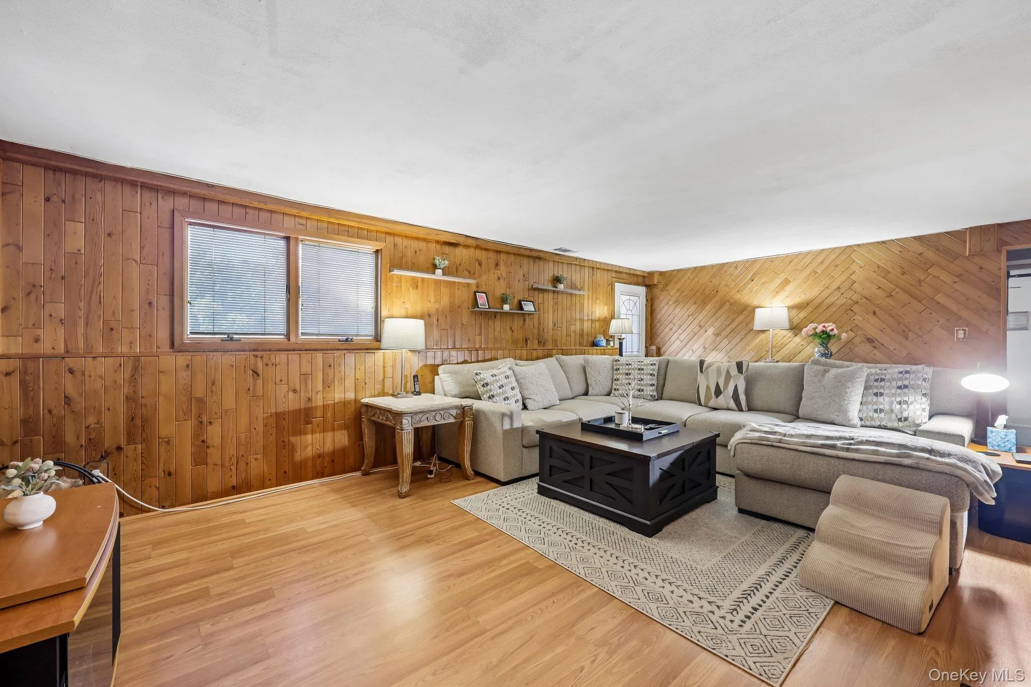 Spacious living area featuring wood-finish flooring, recessed lighting, and wood paneling on walls Spacious living area featuring wood-finish flooring, recessed lighting, and wood paneling on walls