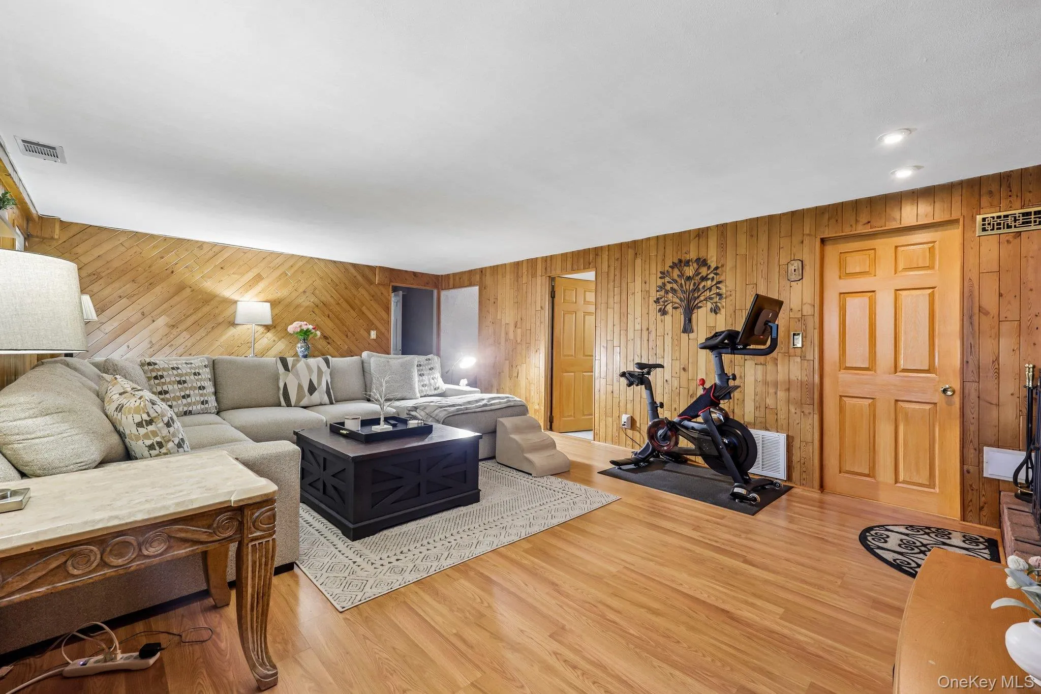 Spacious living area featuring wood-finish flooring, recessed lighting, and wood paneling on walls Spacious living area featuring wood-finish flooring, recessed lighting, and wood paneling on walls