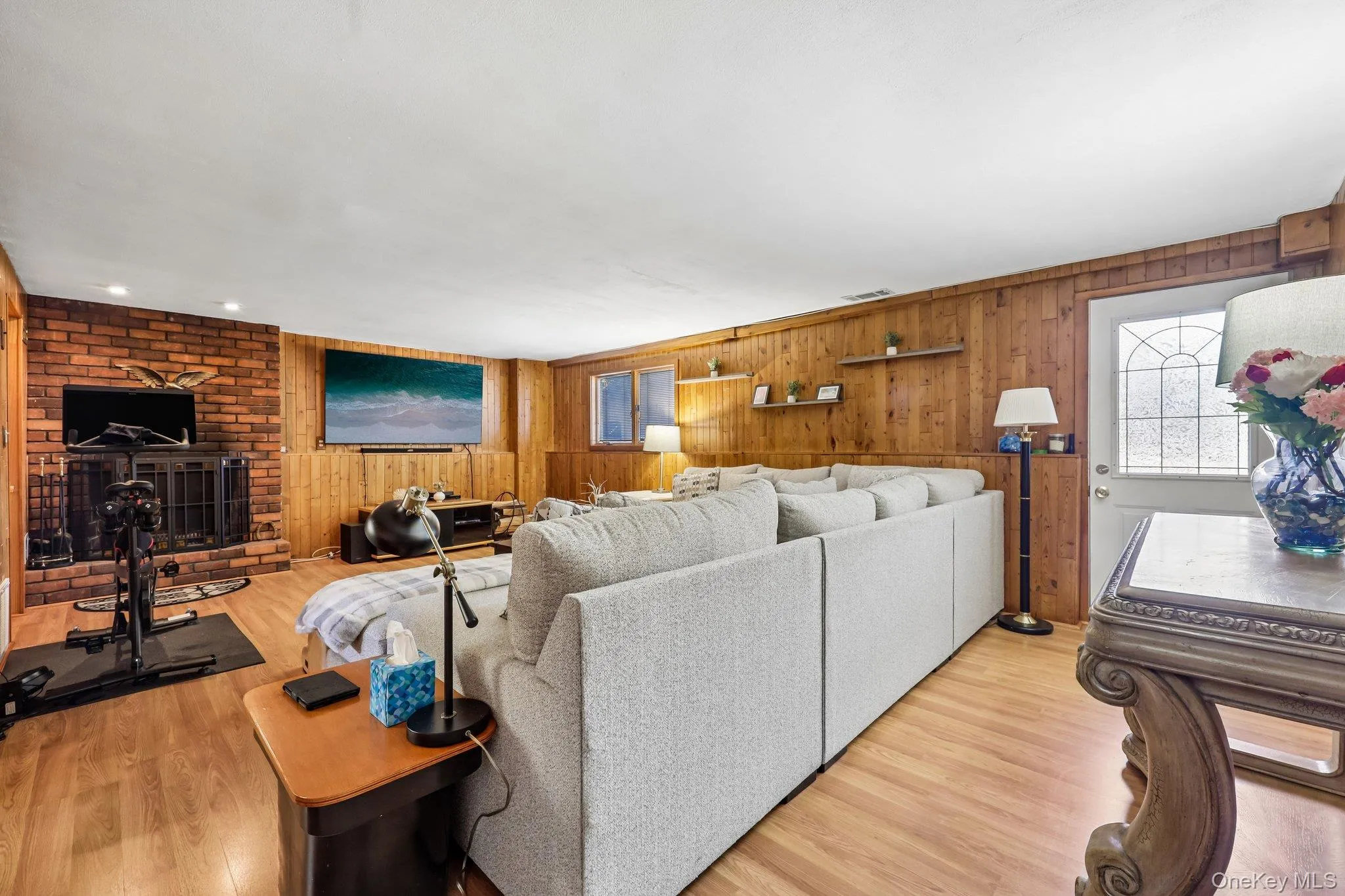 Spacious living area featuring wood-finish flooring, working brick fireplace, and wood paneled walls with walk out to yard Spacious living area featuring wood-finish flooring, working brick fireplace, and wood paneled walls with walk out to yard