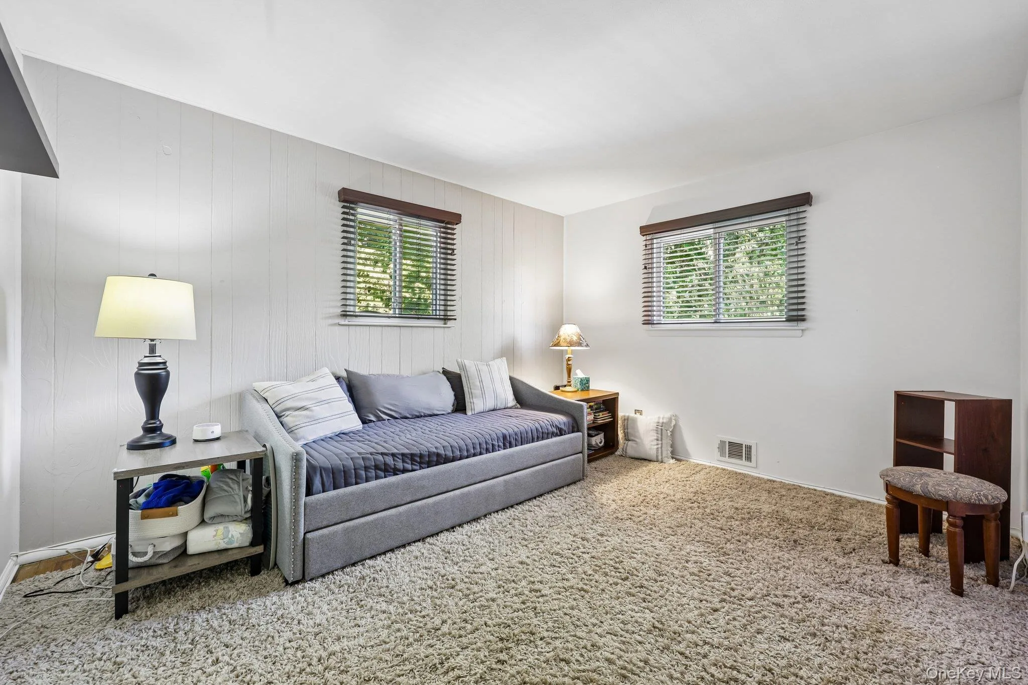 Bright white bedroom with wood paneled wall, carpet over wood floor, closet, & two windows bringing in plenty of light from front and side of home. Bright white bedroom with wood paneled wall, carpet over wood floor, closet, & two windows bringing in plenty of light from front and side of home.