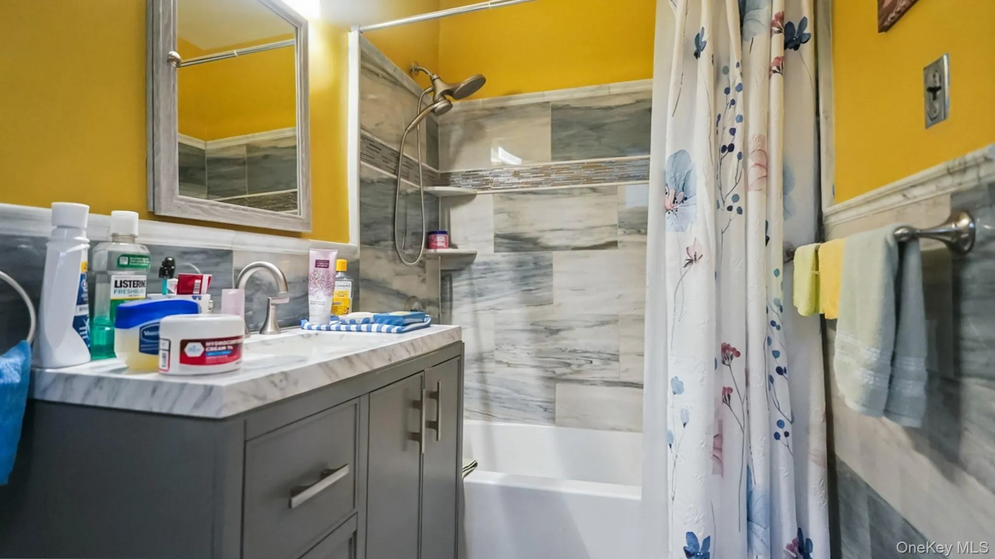 Bathroom featuring a single vanity with a gray cabinet base and a countertop with gray veining, a chrome faucet, and a wall-mounted mirror Bathroom featuring a single vanity with a gray cabinet base and a countertop with gray veining, a chrome faucet, and a wall-mounted mirror