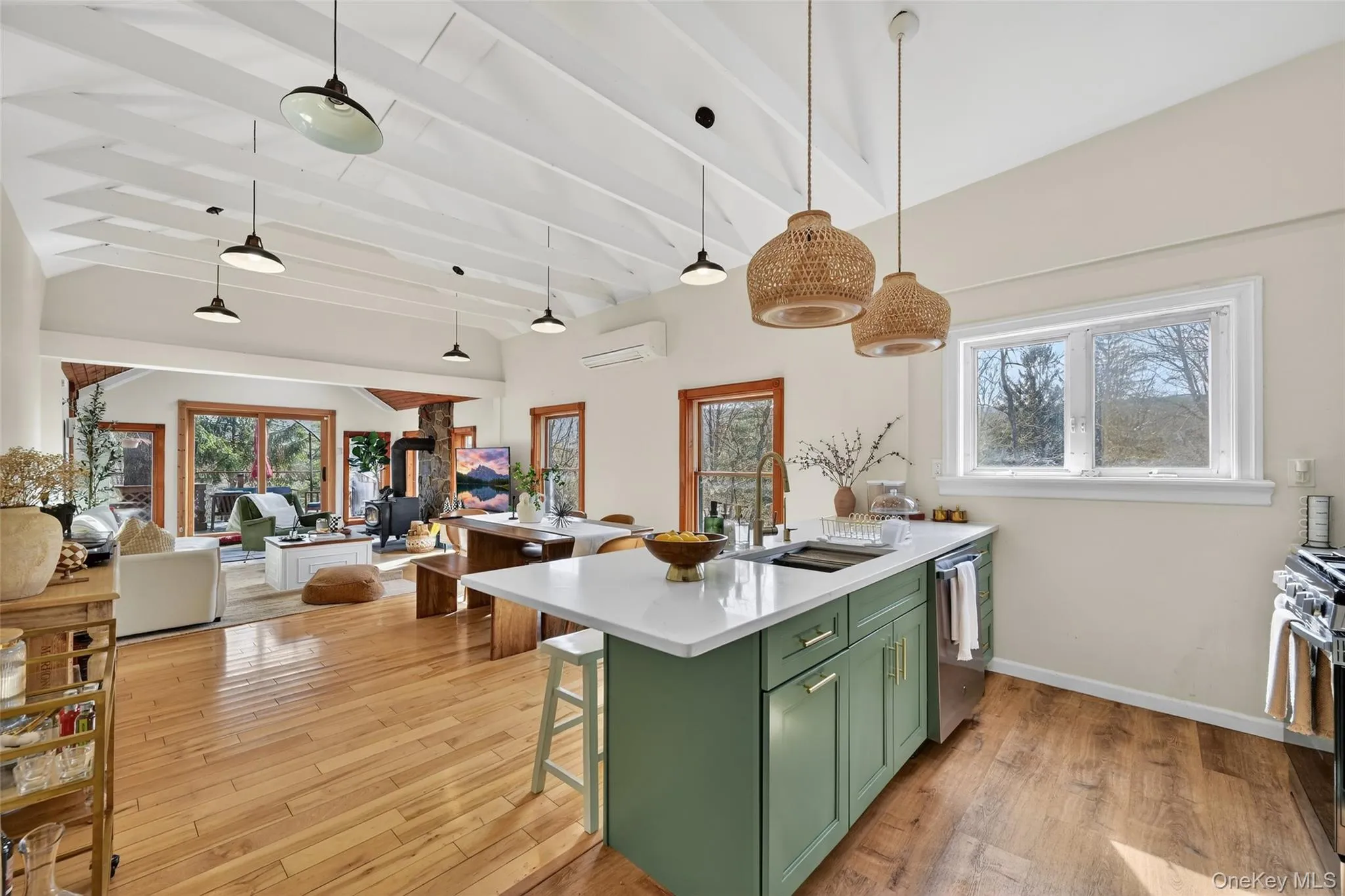 Open-concept living space featuring vaulted ceilings with exposed beams, wood-finish flooring, and a kitchen island with a light green finish and white countertop Open-concept living space featuring vaulted ceilings with exposed beams, wood-finish flooring, and a kitchen island with a light green finish and white countertop
