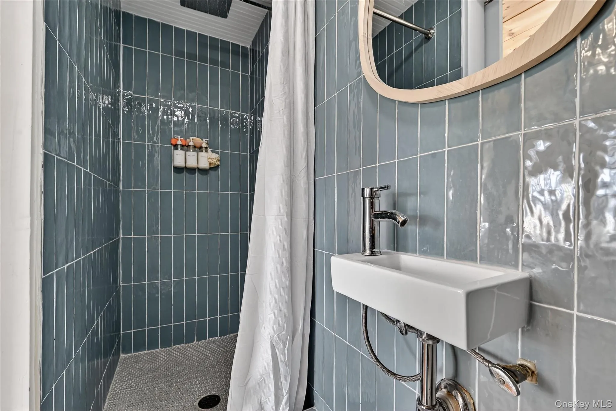 Bathroom featuring a wall-mounted rectangular basin sink with chrome faucet, a wooden framed mirror, and vertical blue subway tile shower surround with a white shower curtain Bathroom featuring a wall-mounted rectangular basin sink with chrome faucet, a wooden framed mirror, and vertical blue subway tile shower surround with a white shower curtain