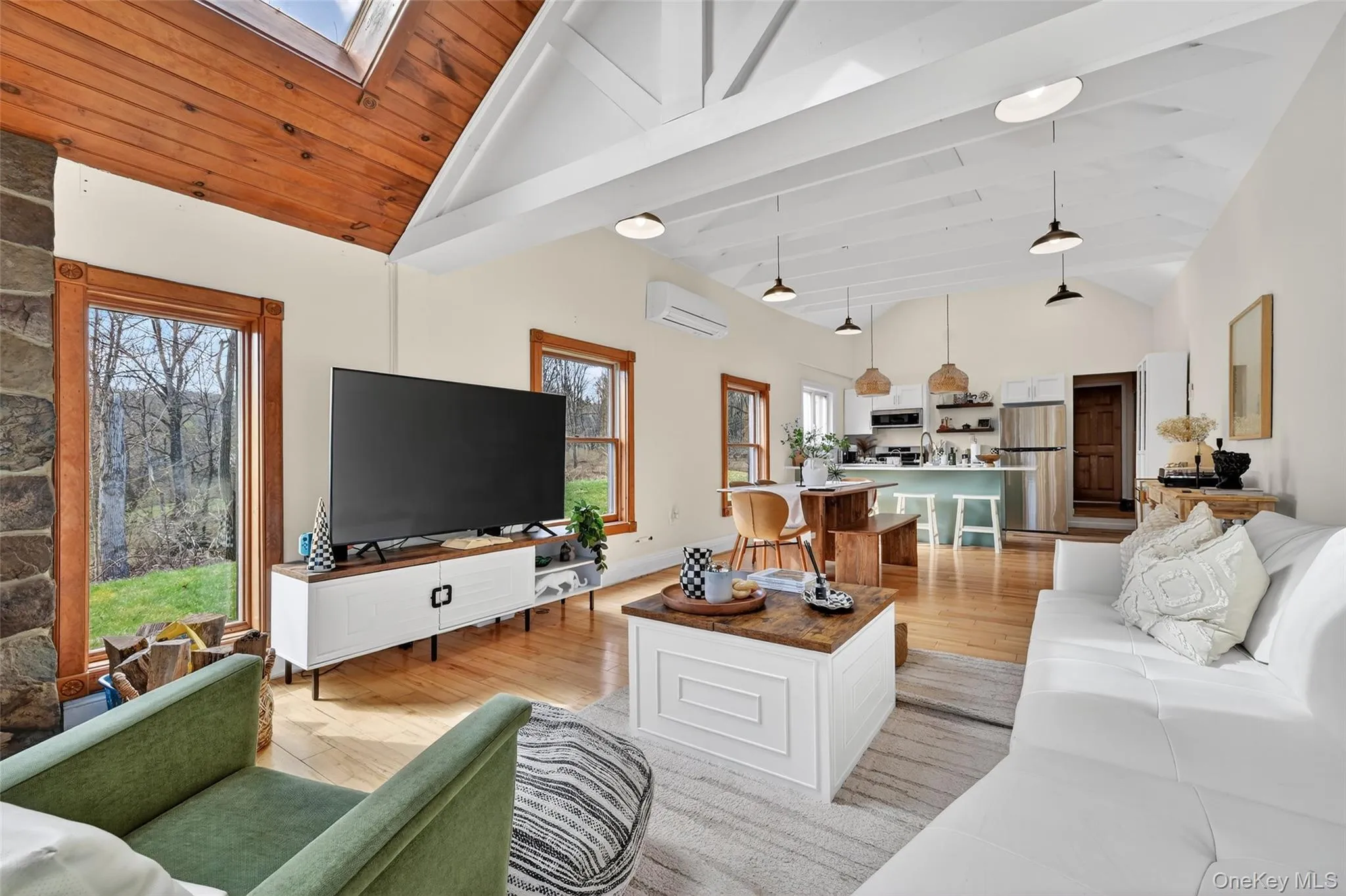 Open concept living area featuring vaulted ceilings with exposed beams, wood-finish flooring, and a stone-clad fireplace Open concept living area featuring vaulted ceilings with exposed beams, wood-finish flooring, and a stone-clad fireplace