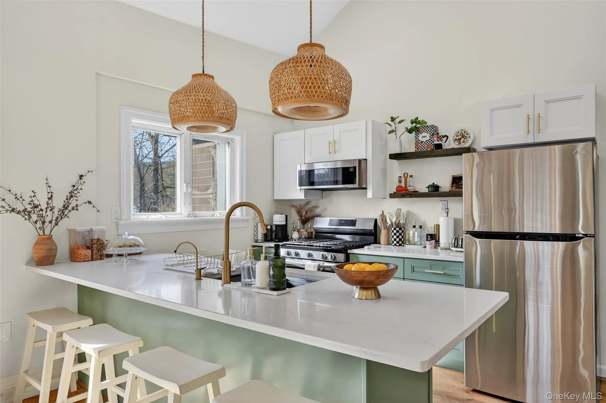 Bright kitchen featuring a peninsula with a light-toned countertop, a window above the sink, stainless steel appliances, white upper cabinetry, and open shelving Bright kitchen featuring a peninsula with a light-toned countertop, a window above the sink, stainless steel appliances, white upper cabinetry, and open shelving
