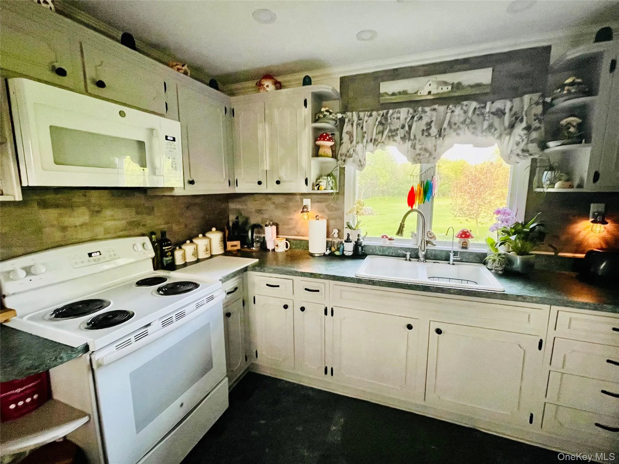 Kitchen with grey cabinetry, electric stove, microwave, double sink and window view. Kitchen with grey cabinetry, electric stove, microwave, double sink and window view.
