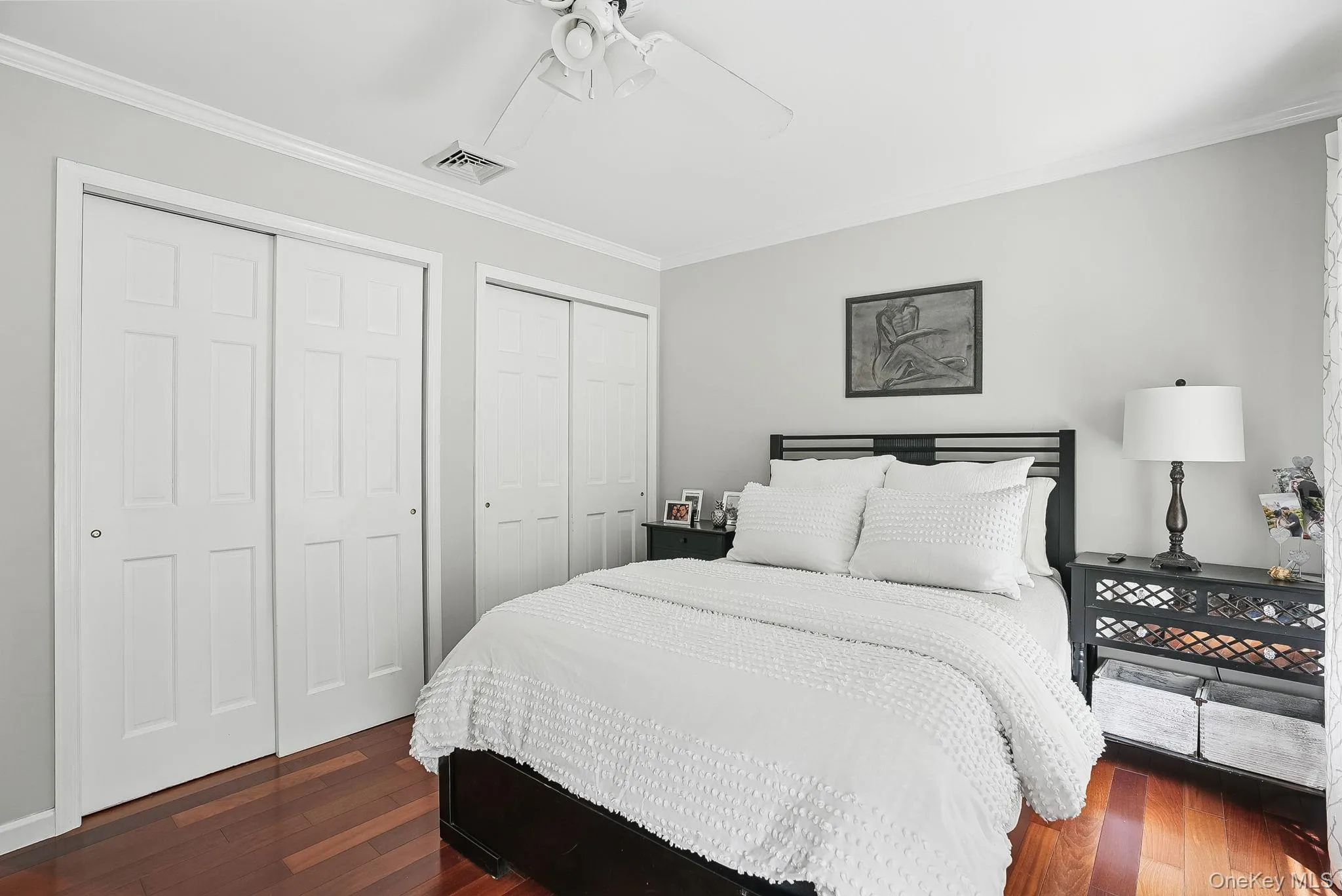 Bedroom with multiple closets, dark wood-style floors, crown molding, and ceiling fan Bedroom with multiple closets, dark wood-style floors, crown molding, and ceiling fan