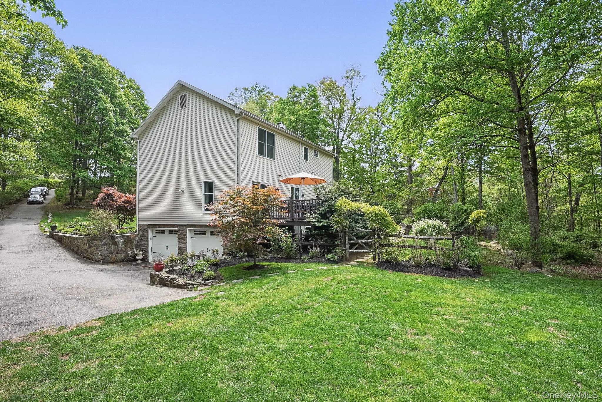 View of property exterior featuring an attached garage, a lawn, a wooden deck, and driveway View of property exterior featuring an attached garage, a lawn, a wooden deck, and driveway