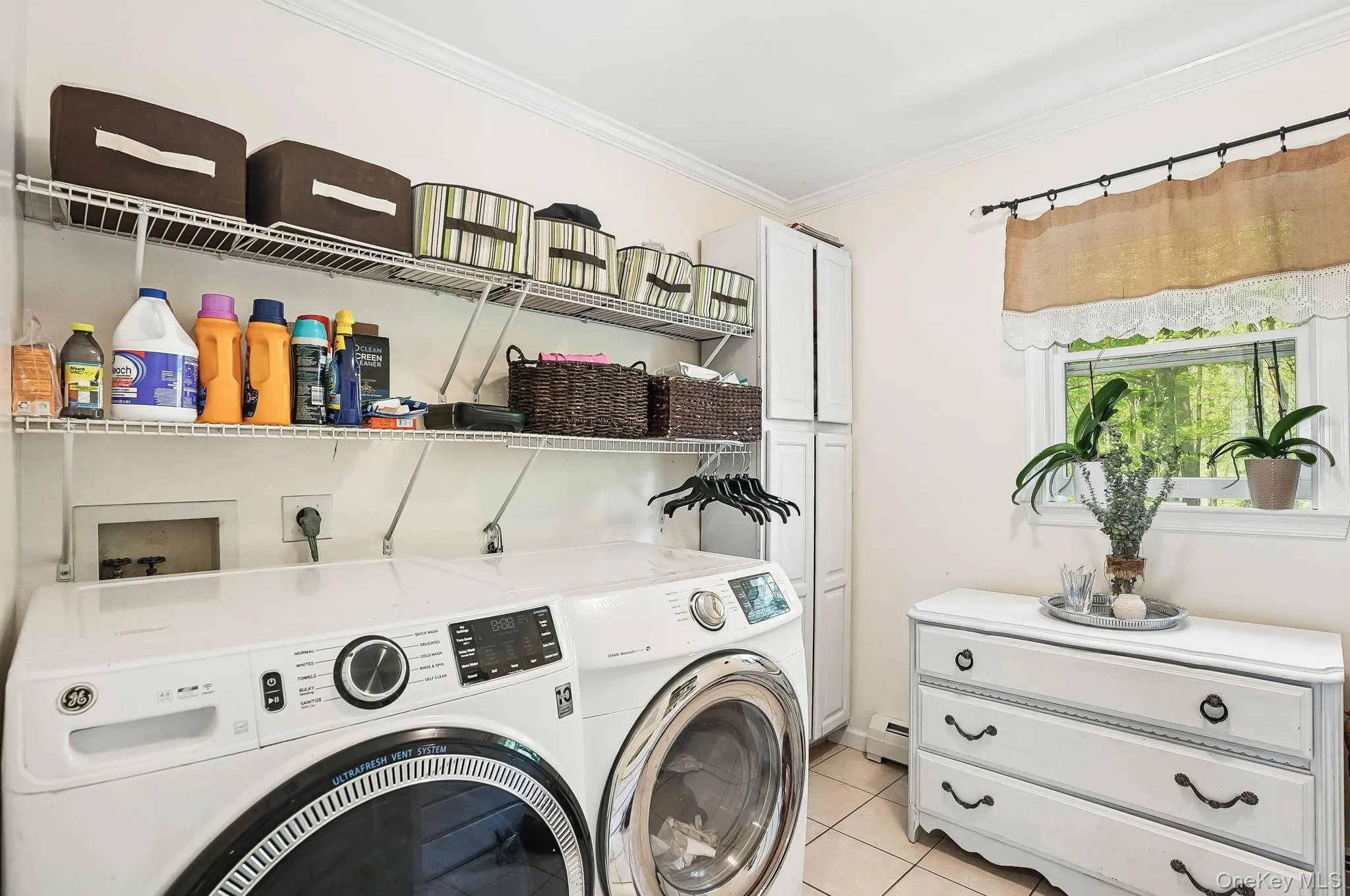 Laundry room featuring separate washer and dryer, ornamental molding, light tile patterned flooring, cabinet space, and a baseboard heating unit Laundry room featuring separate washer and dryer, ornamental molding, light tile patterned flooring, cabinet space, and a baseboard heating unit