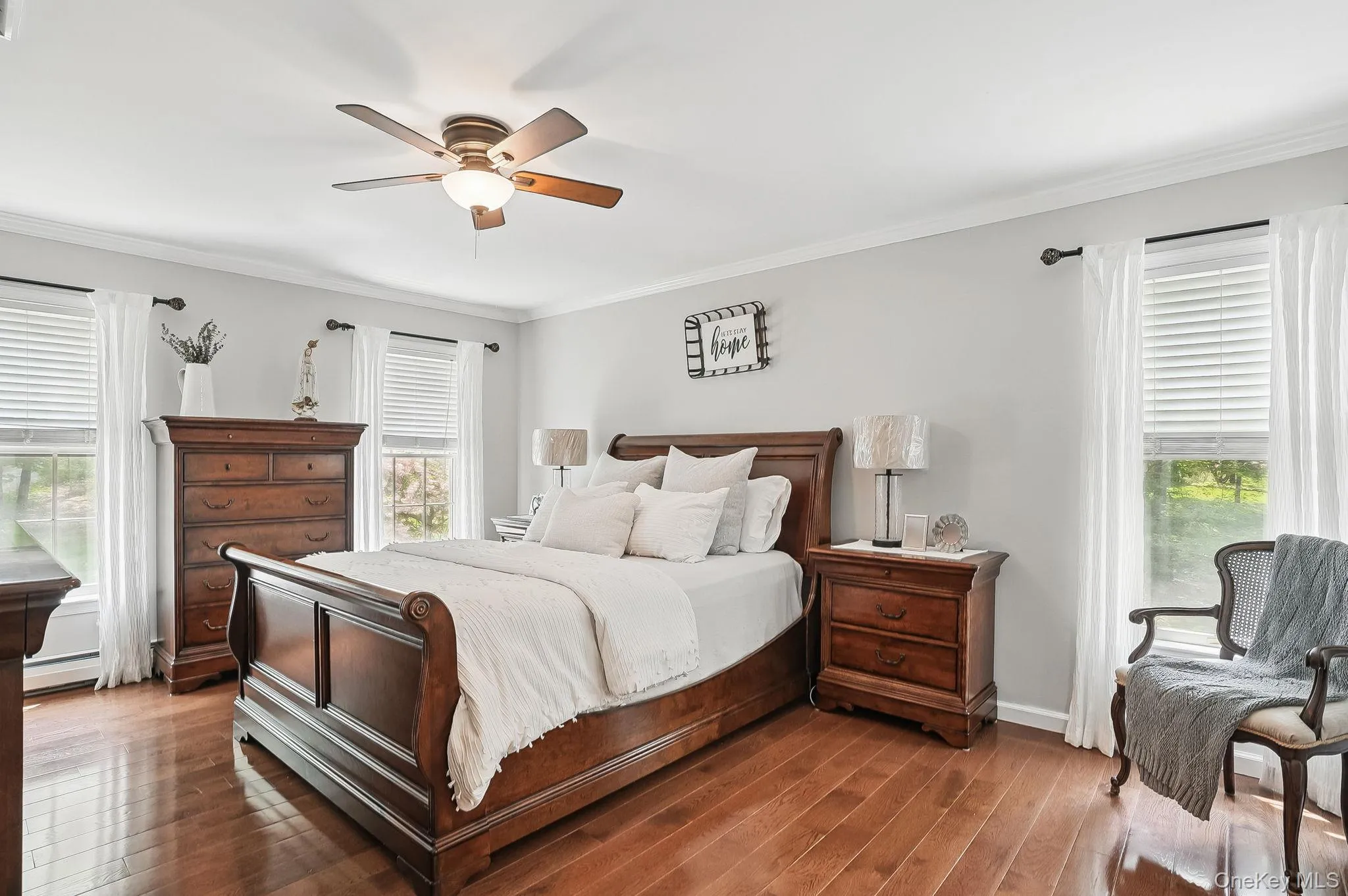 Bedroom featuring a baseboard radiator, wood finished floors, crown molding, a ceiling fan, and baseboards Bedroom featuring a baseboard radiator, wood finished floors, crown molding, a ceiling fan, and baseboards