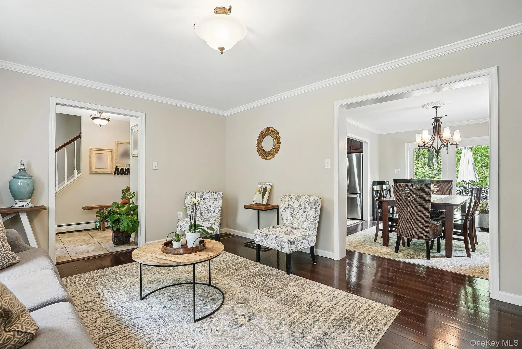 Living room featuring baseboard heating, a chandelier, crown molding, stairway, and hardwood / wood-style flooring Living room featuring baseboard heating, a chandelier, crown molding, stairway, and hardwood / wood-style flooring