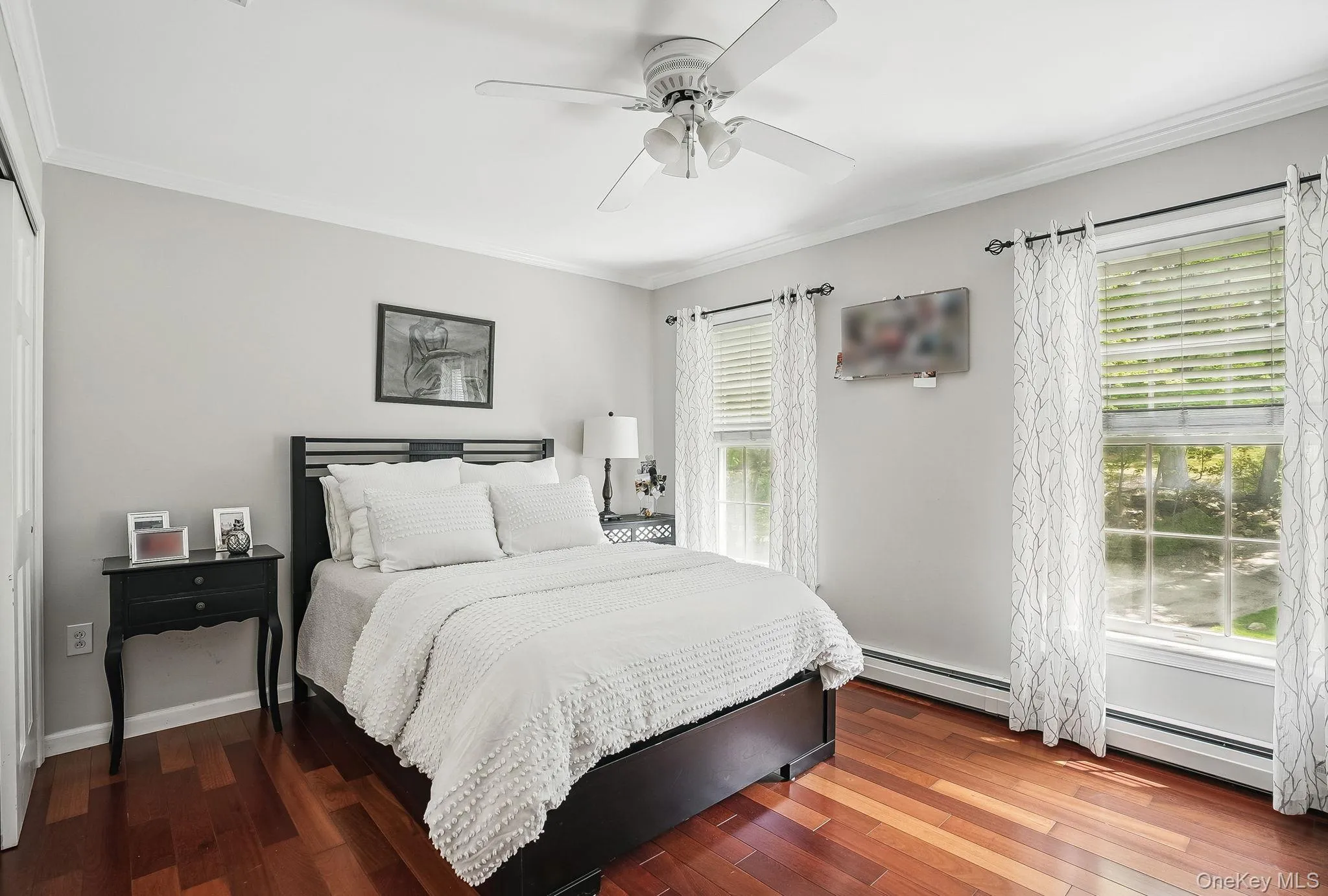 Bedroom featuring ornamental molding, a baseboard heating unit, wood-type flooring, and multiple windows Bedroom featuring ornamental molding, a baseboard heating unit, wood-type flooring, and multiple windows
