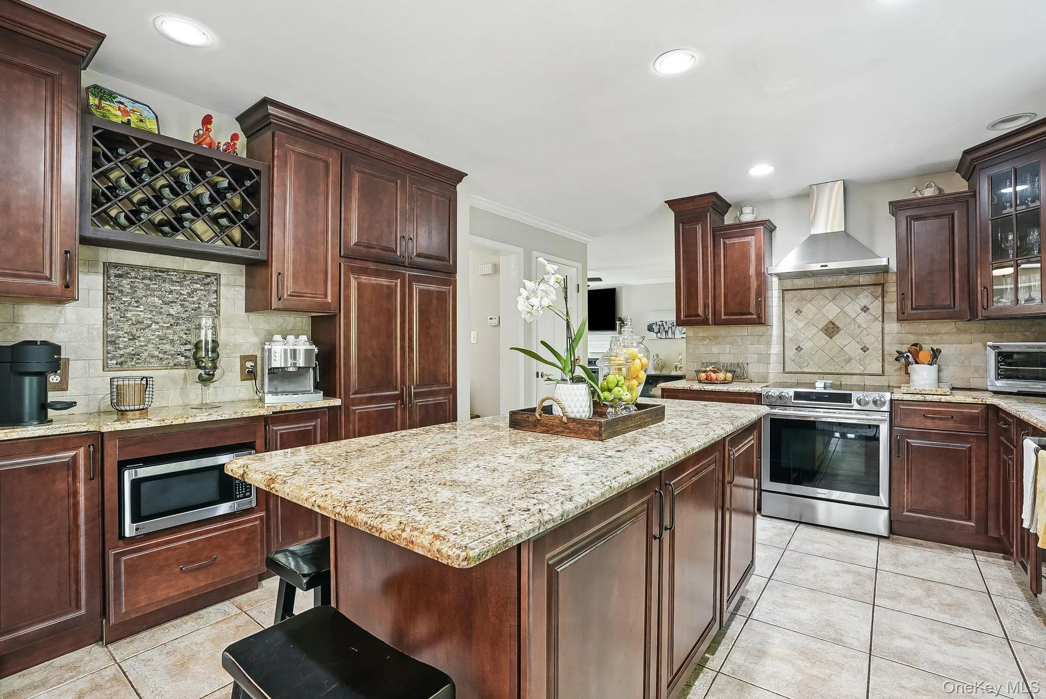 Kitchen featuring stainless steel appliances, wall chimney range hood, light tile patterned flooring, tasteful backsplash, and ornamental molding Kitchen featuring stainless steel appliances, wall chimney range hood, light tile patterned flooring, tasteful backsplash, and ornamental molding