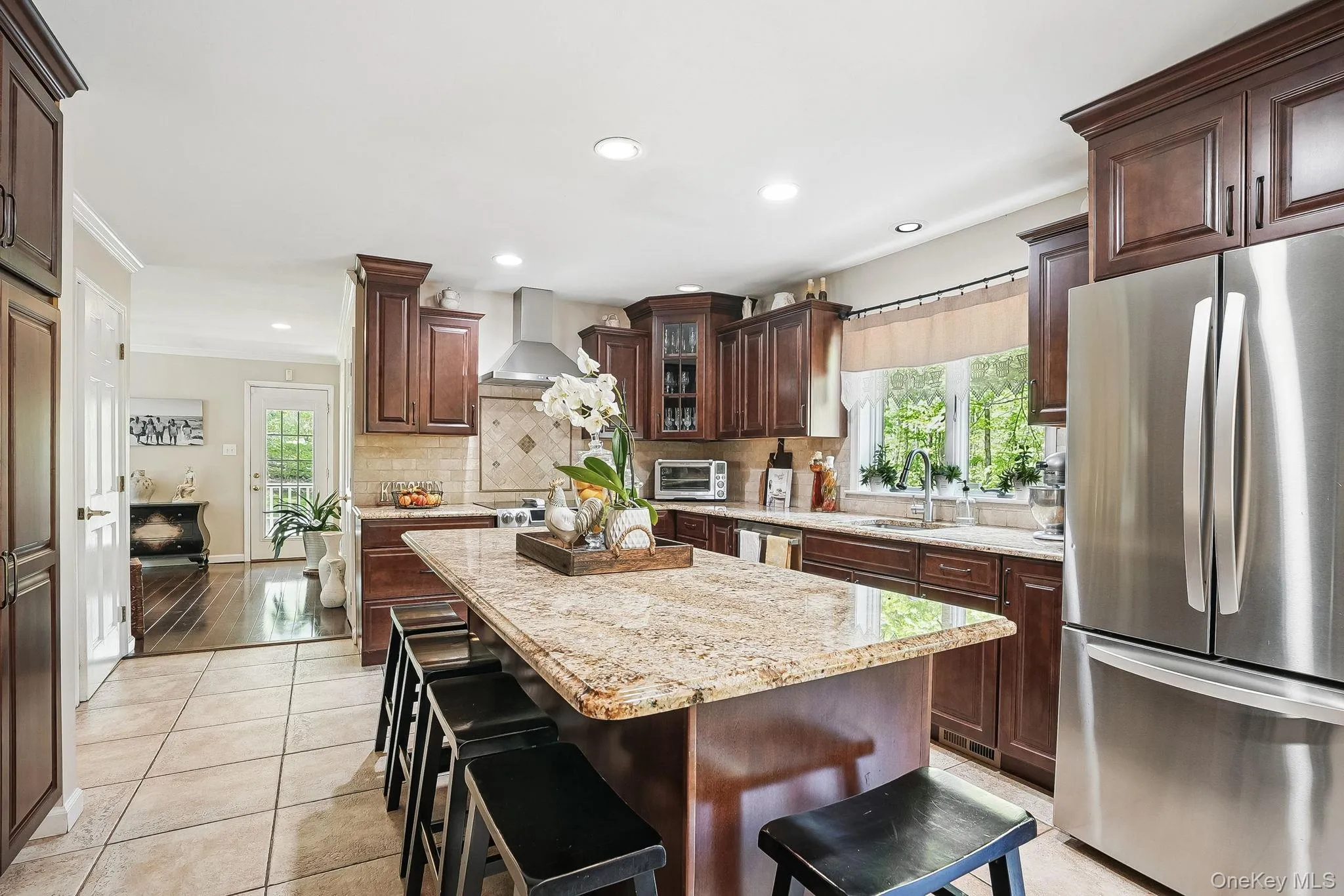 Kitchen featuring freestanding refrigerator, wall chimney range hood, a sink, tasteful backsplash, and a center island Kitchen featuring freestanding refrigerator, wall chimney range hood, a sink, tasteful backsplash, and a center island