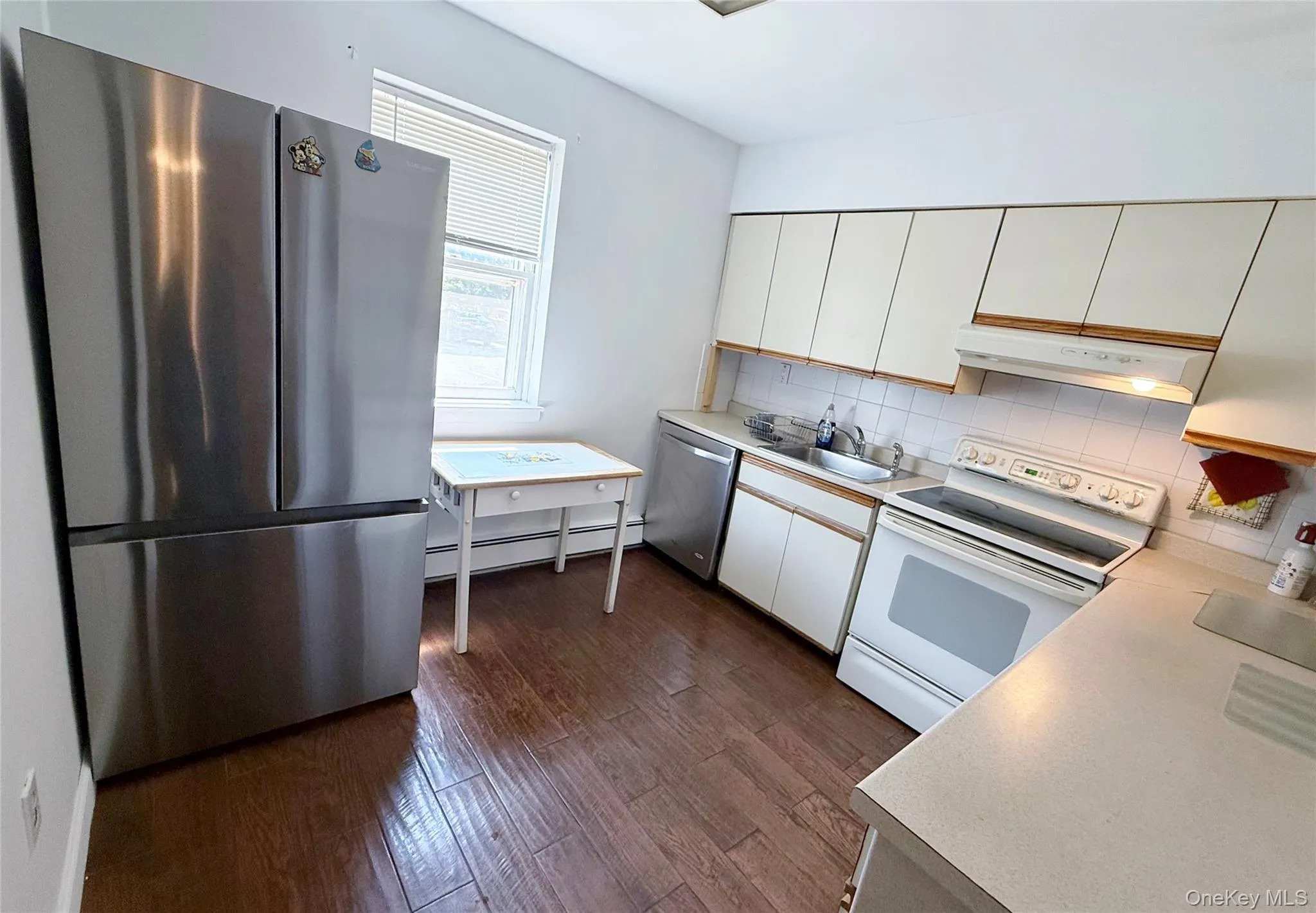 Kitchen featuring wood-finish flooring, stainless steel French door refrigerator, white cabinetry, integrated dishwasher, and white tile backsplash Kitchen featuring wood-finish flooring, stainless steel French door refrigerator, white cabinetry, integrated dishwasher, and white tile backsplash