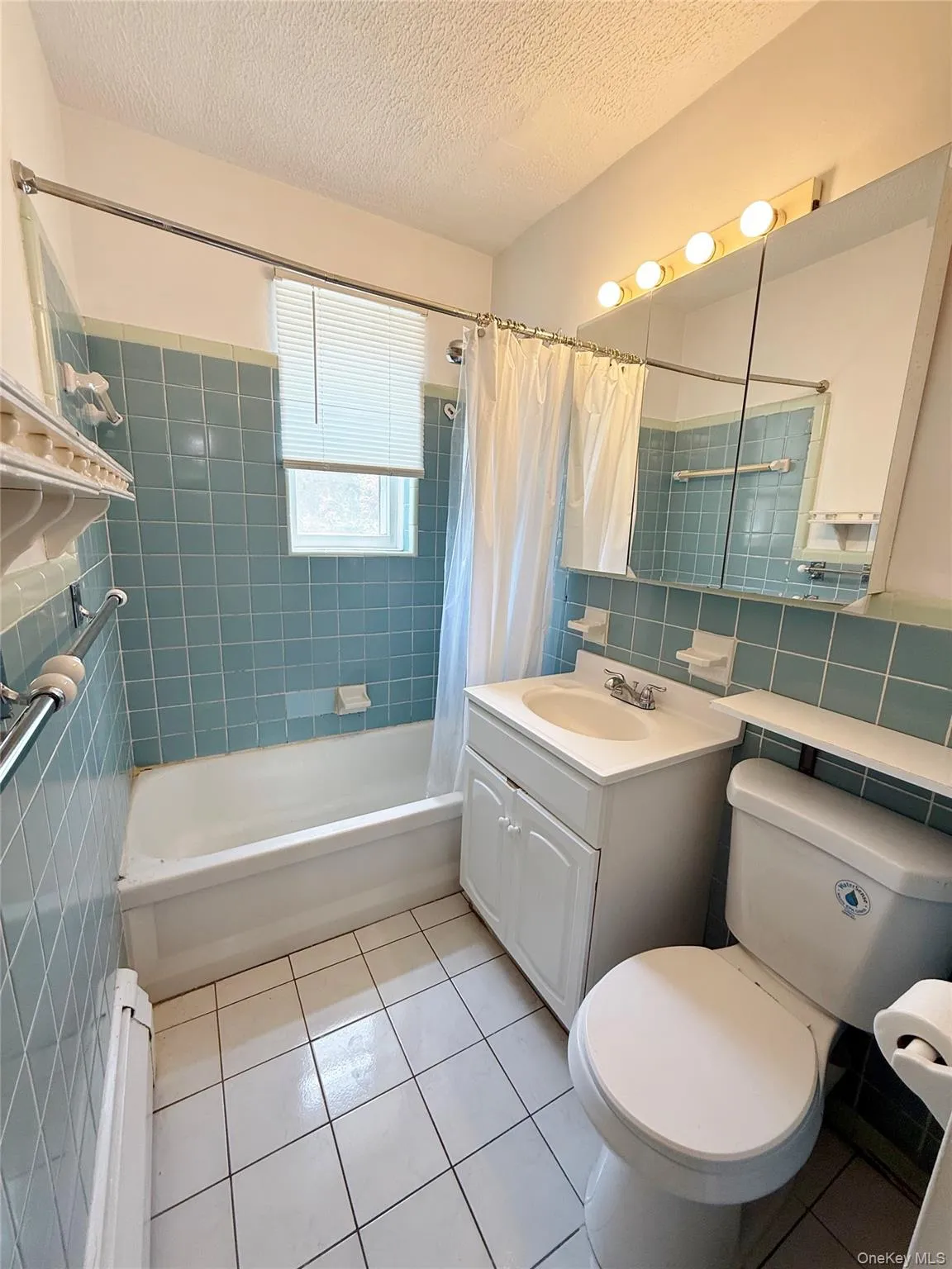 Bathroom featuring a white bathtub, blue tiled walls, white tile flooring, a single vanity with storage, and a mirrored medicine cabinet with integrated lighting Bathroom featuring a white bathtub, blue tiled walls, white tile flooring, a single vanity with storage, and a mirrored medicine cabinet with integrated lighting