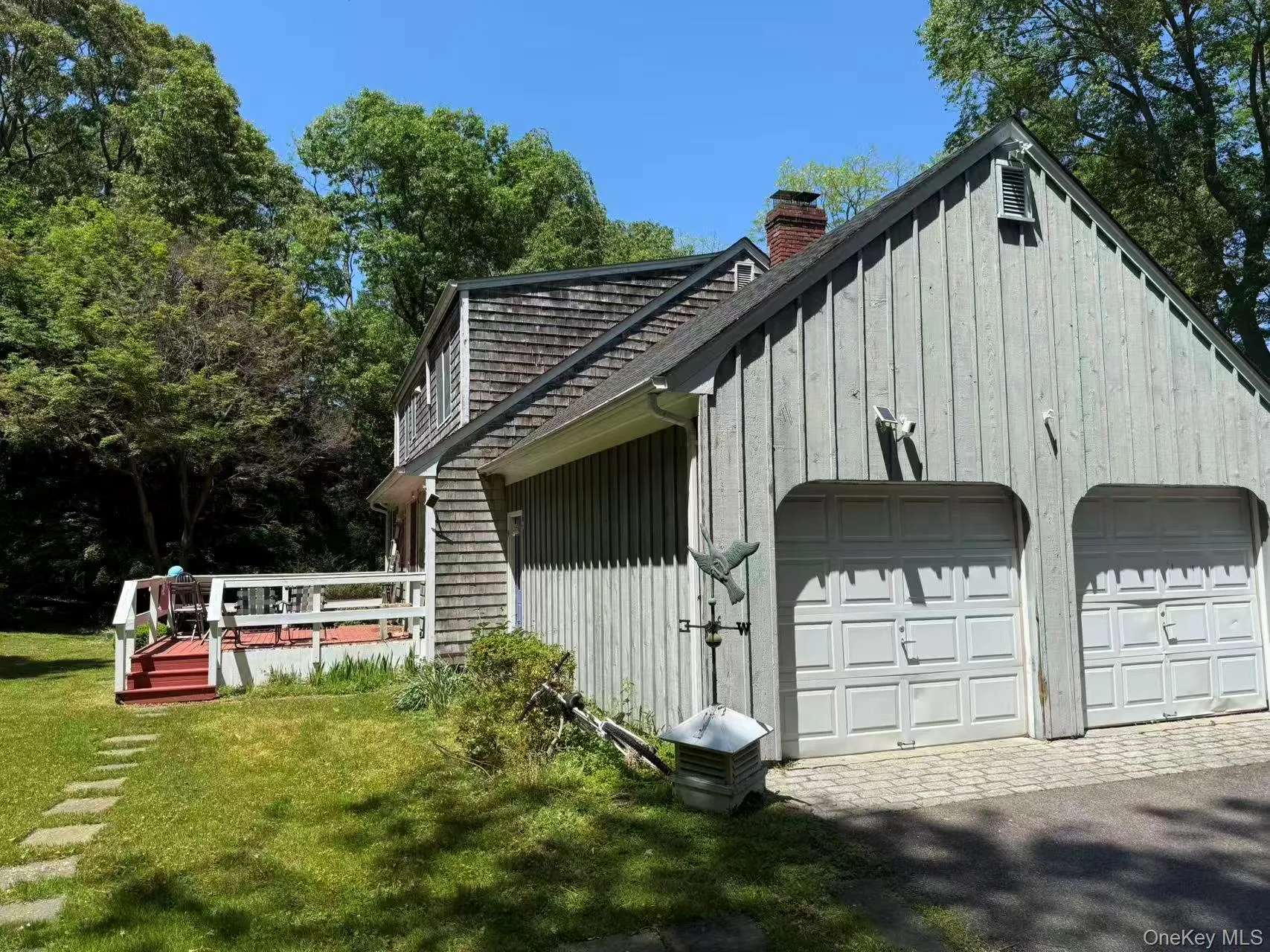 Exterior featuring vertical siding and shingle accents, a two-car garage with panel doors, a red-painted deck with white railings, and a stone paver walkway Exterior featuring vertical siding and shingle accents, a two-car garage with panel doors, a red-painted deck with white railings, and a stone paver walkway