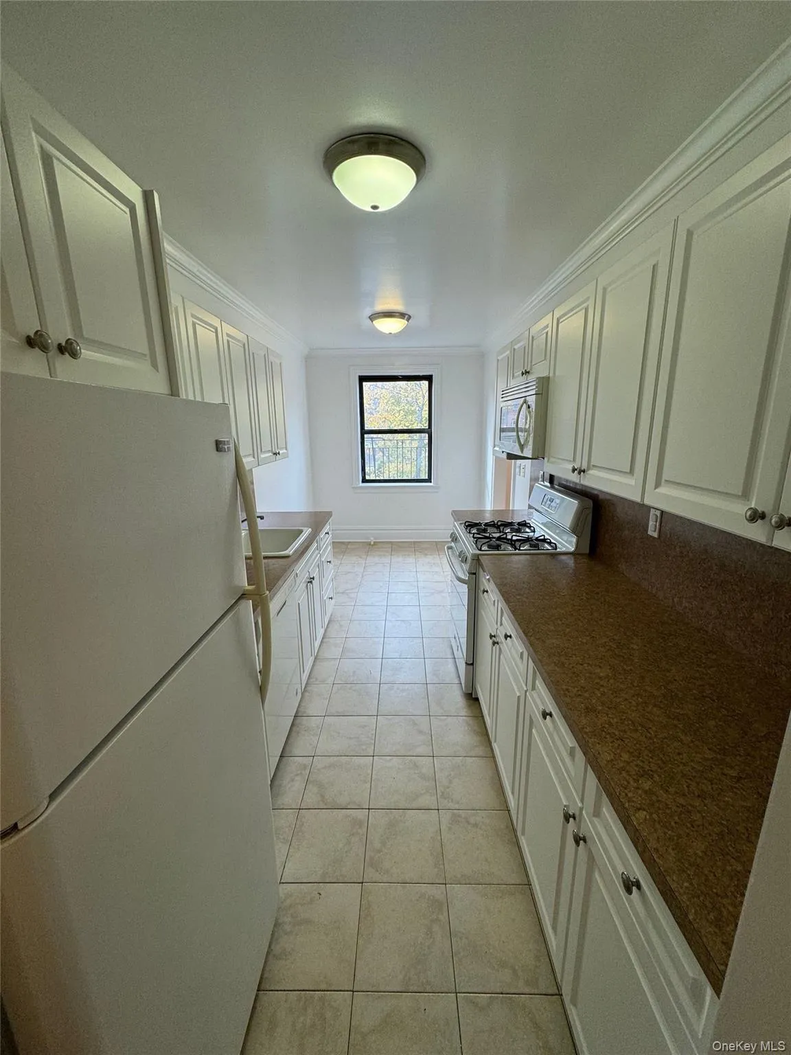 Kitchen with white appliances, white cabinets, ornamental molding, light tile patterned floors, and dark stone counters Kitchen with white appliances, white cabinets, ornamental molding, light tile patterned floors, and dark stone counters