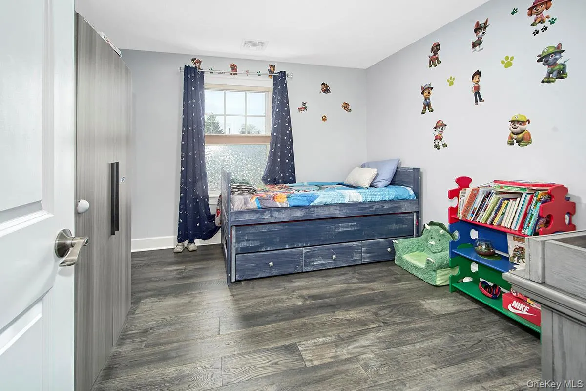 Room featuring wood-finish flooring, a double window with blinds, and a built-in wardrobe with contemporary hardware Room featuring wood-finish flooring, a double window with blinds, and a built-in wardrobe with contemporary hardware