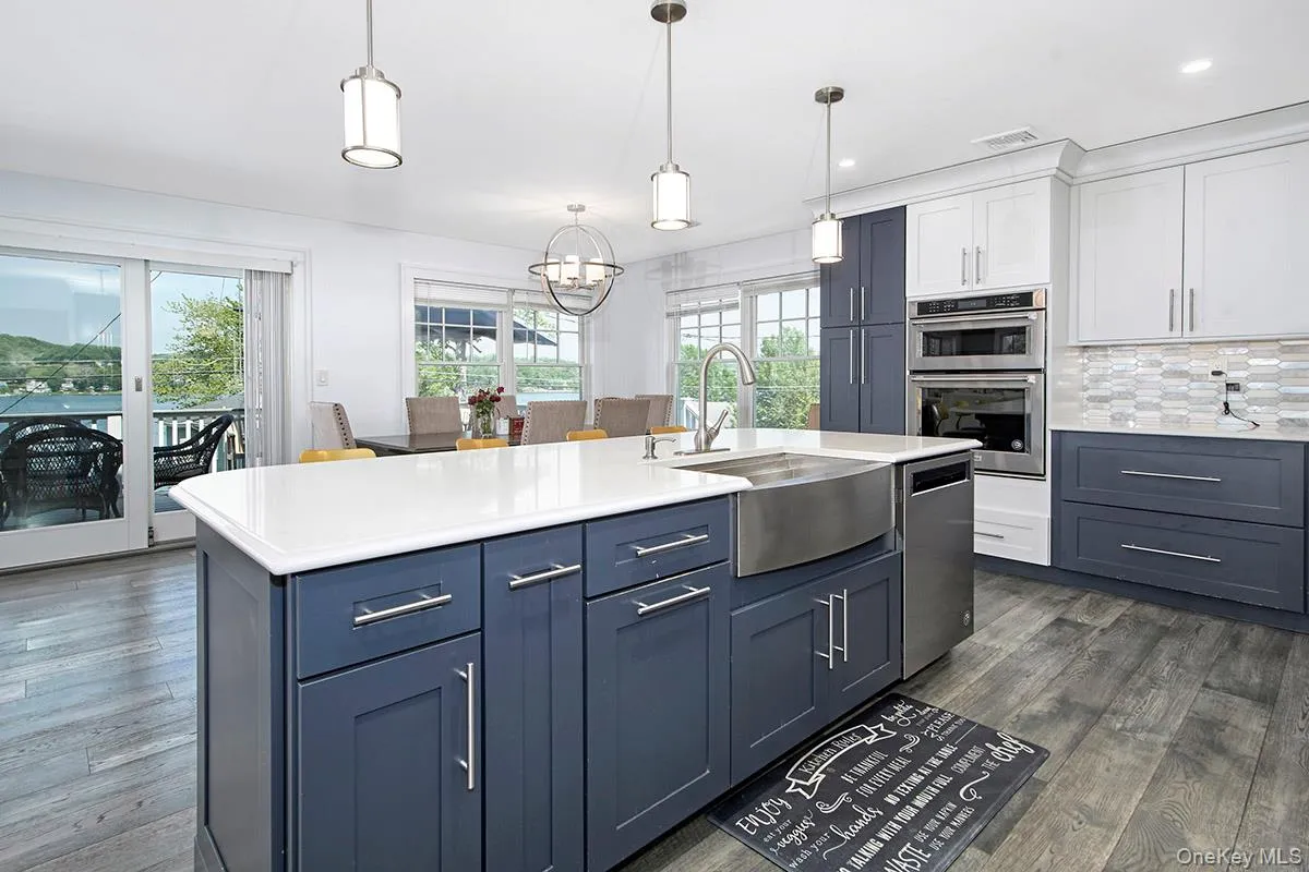 Kitchen featuring a large island with a farmhouse sink, stainless steel appliances, two-tone cabinetry, and wood-finish flooring Kitchen featuring a large island with a farmhouse sink, stainless steel appliances, two-tone cabinetry, and wood-finish flooring