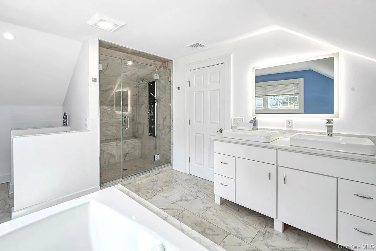 Spacious bathroom featuring a dual vanity with vessel sinks, an illuminated mirror, a glass-enclosed shower with a built-in bench, and a large soaking tub Spacious bathroom featuring a dual vanity with vessel sinks, an illuminated mirror, a glass-enclosed shower with a built-in bench, and a large soaking tub
