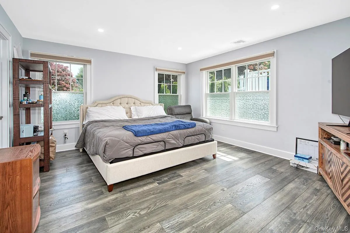 Spacious room featuring wood-finish flooring, two large windows, recessed ceiling lighting, and light-toned wall finishes Spacious room featuring wood-finish flooring, two large windows, recessed ceiling lighting, and light-toned wall finishes