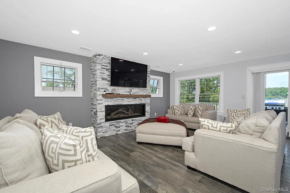 Spacious living area featuring plank wood-finish flooring, a stone-clad fireplace with a wood mantle, and recessed lighting Spacious living area featuring plank wood-finish flooring, a stone-clad fireplace with a wood mantle, and recessed lighting
