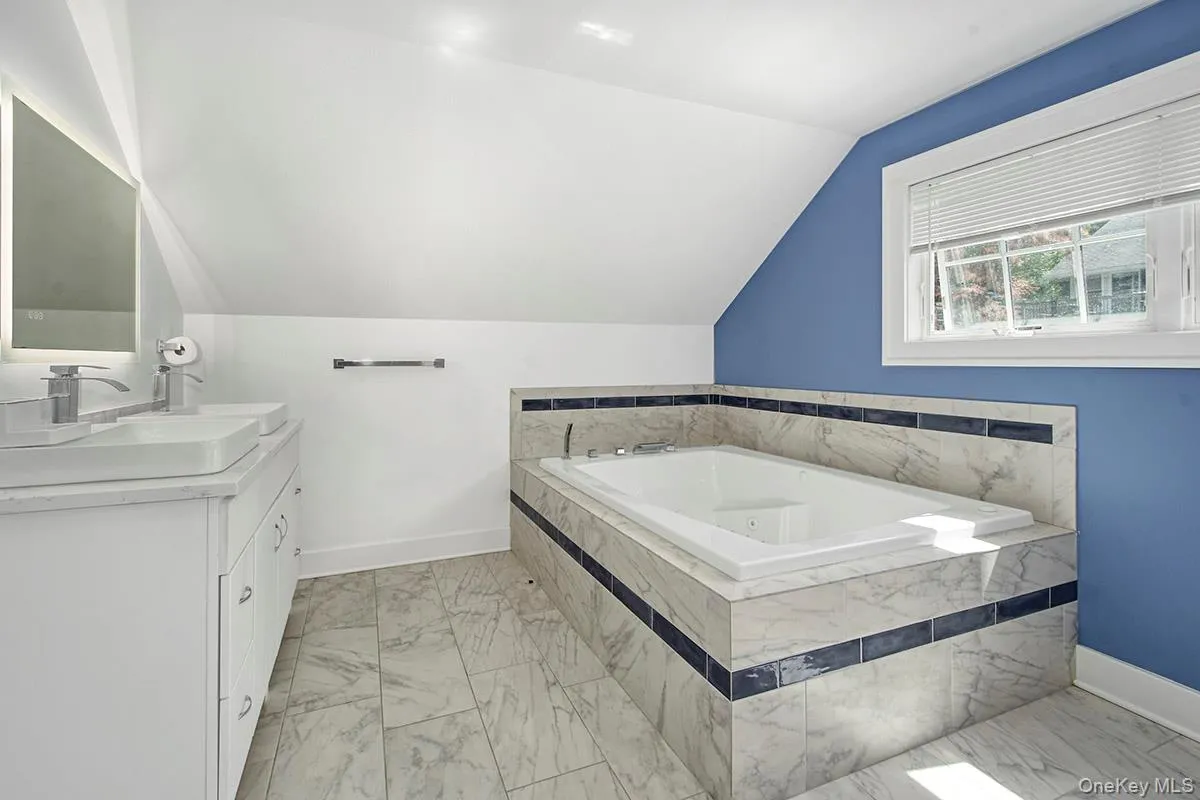 Jacuzzi tub with integrated tiling, dual vessel sinks, modern vanity with cabinet storage, tiled flooring, and an illuminated mirror Jacuzzi tub with integrated tiling, dual vessel sinks, modern vanity with cabinet storage, tiled flooring, and an illuminated mirror