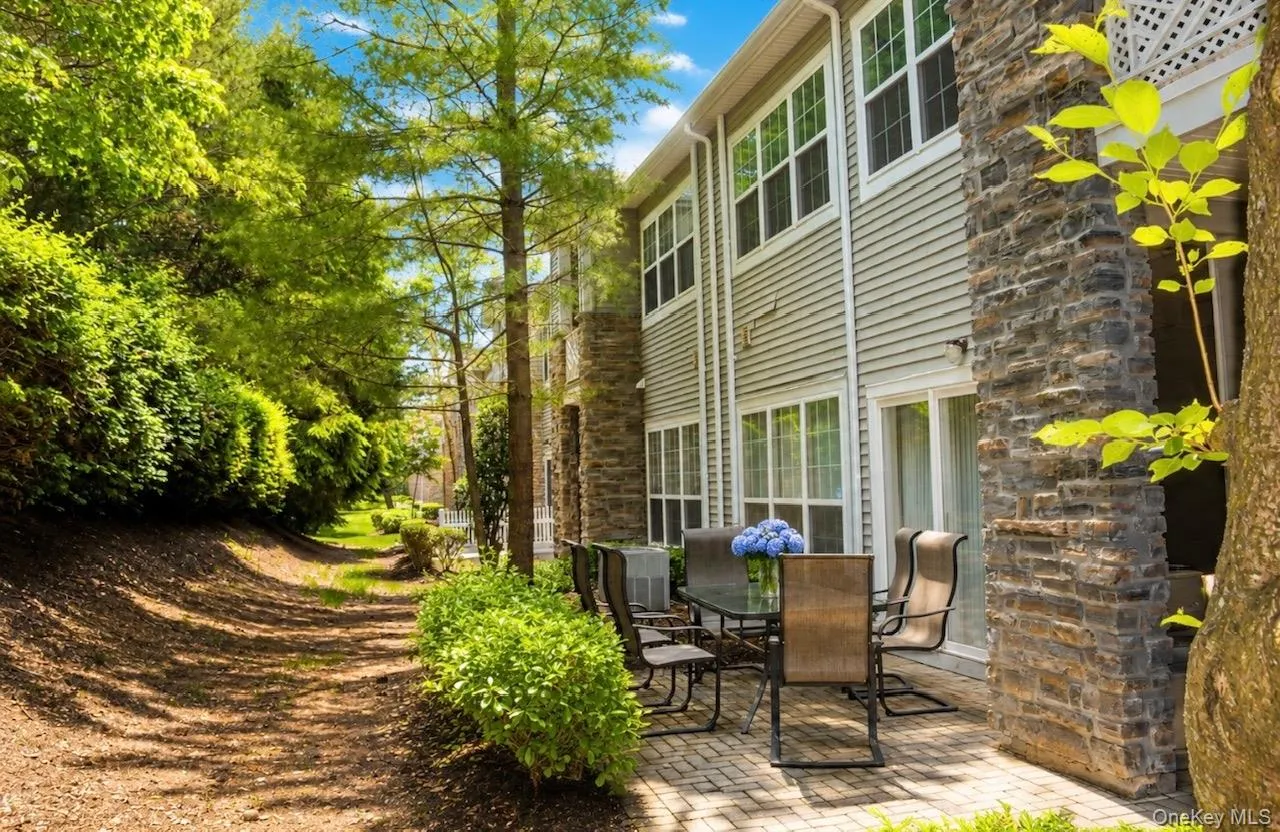 Expansive paver patio bordered by mature landscaping and a natural accents, featuring siding and stone exterior, sliding glass door, and multiple large windows Expansive paver patio bordered by mature landscaping and a natural accents, featuring siding and stone exterior, sliding glass door, and multiple large windows