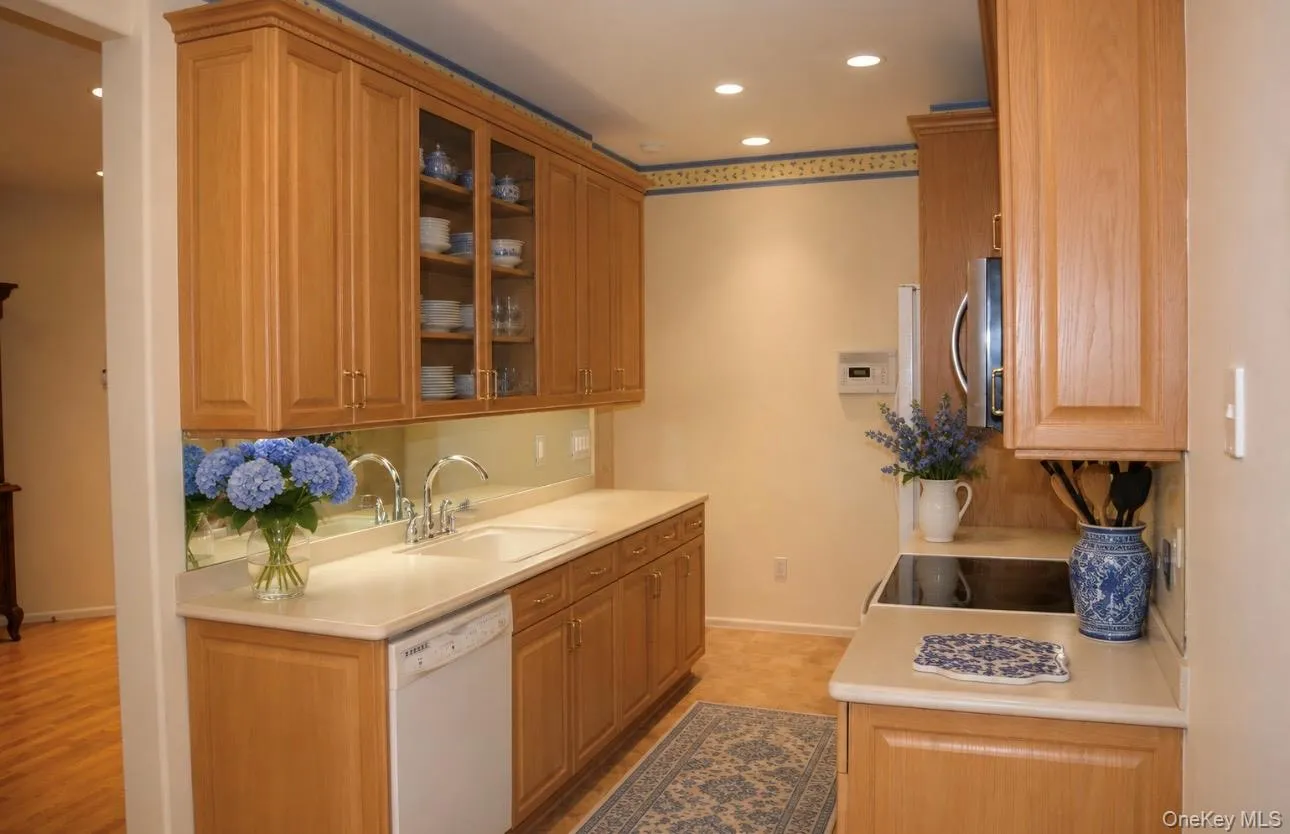 Kitchen featuring light wood cabinetry, glass-front upper cabinets, light countertops, and a built-in electric stovetop Kitchen featuring light wood cabinetry, glass-front upper cabinets, light countertops, and a built-in electric stovetop