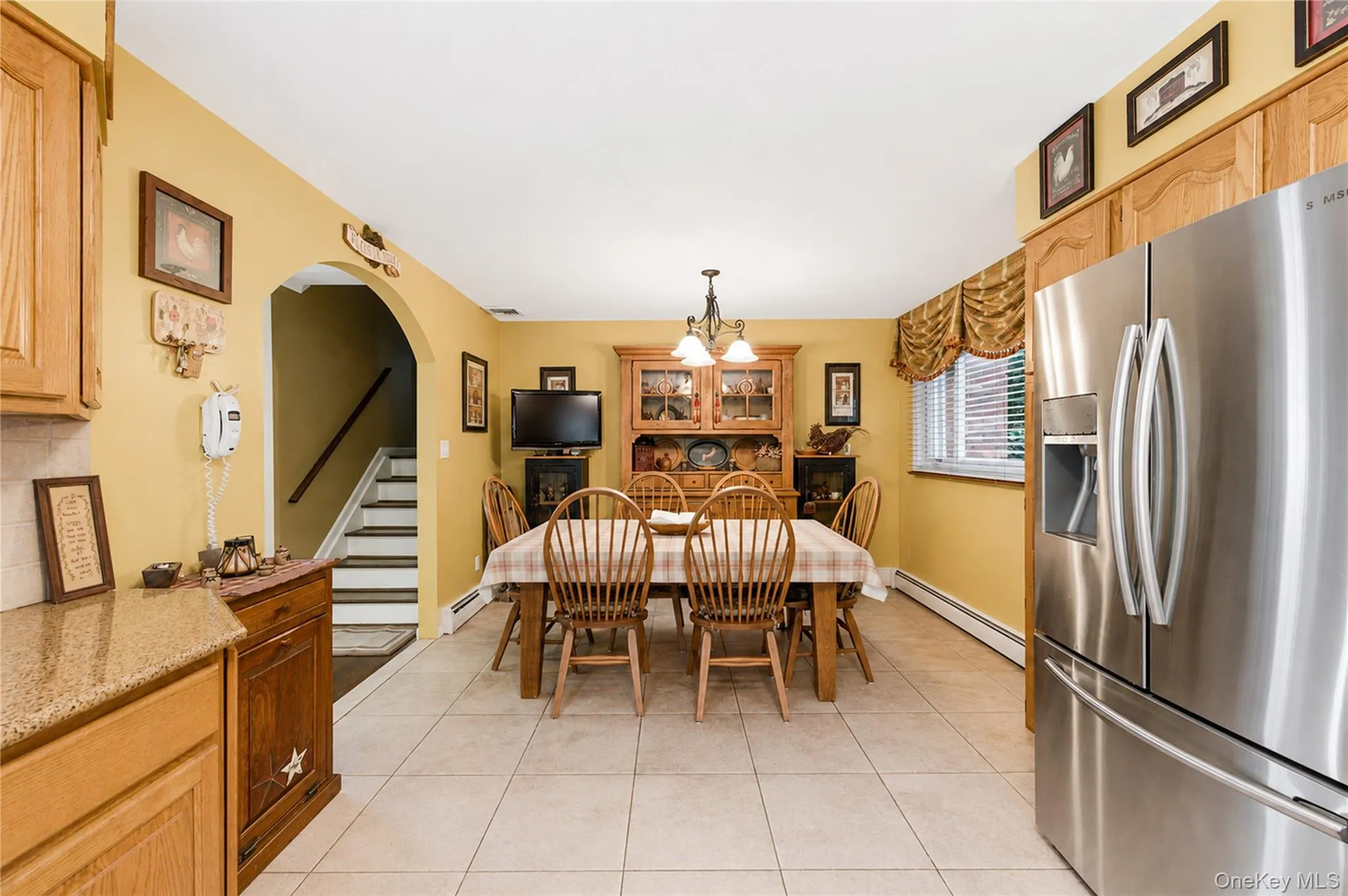 Dining area featuring tile flooring, a large window with blinds, and an arched entry to a staircase Dining area featuring tile flooring, a large window with blinds, and an arched entry to a staircase