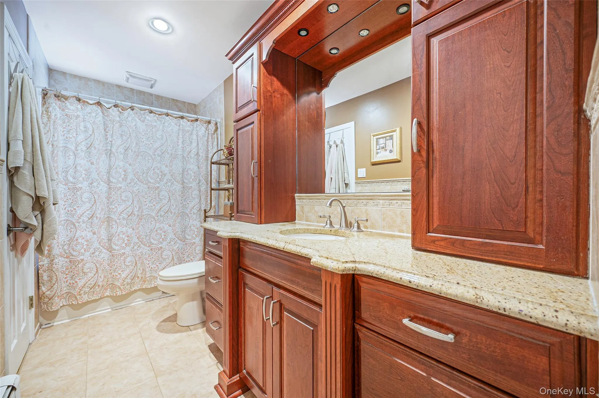 Bathroom featuring a cherry wood-finish vanity with a light speckled countertop, recessed lighting. Bathroom featuring a cherry wood-finish vanity with a light speckled countertop, recessed lighting.