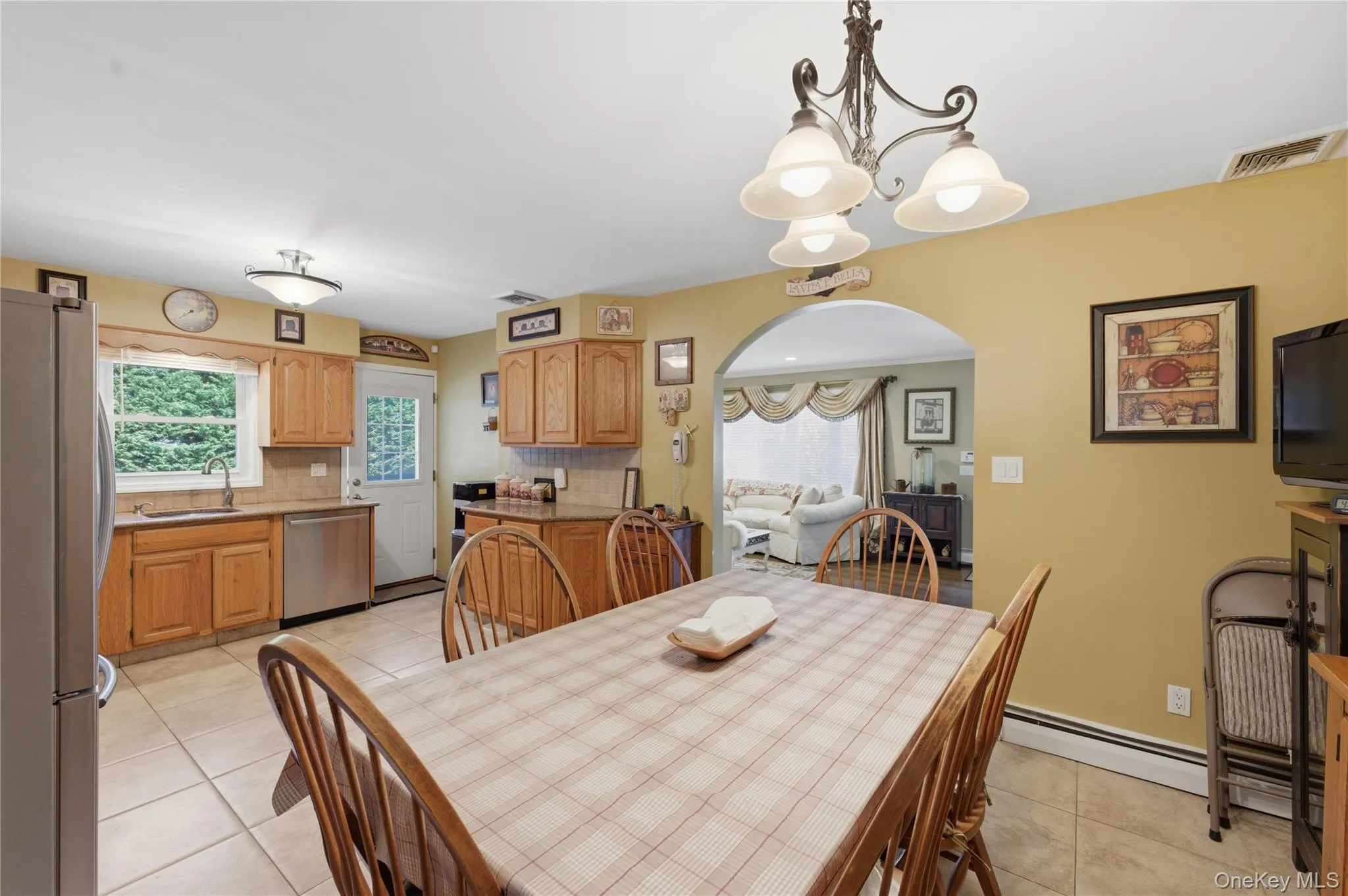 Eat-in kitchen featuring wood cabinetry, stainless steel appliances, tiled flooring, an arched doorway, and a decorative chandelier Eat-in kitchen featuring wood cabinetry, stainless steel appliances, tiled flooring, an arched doorway, and a decorative chandelier