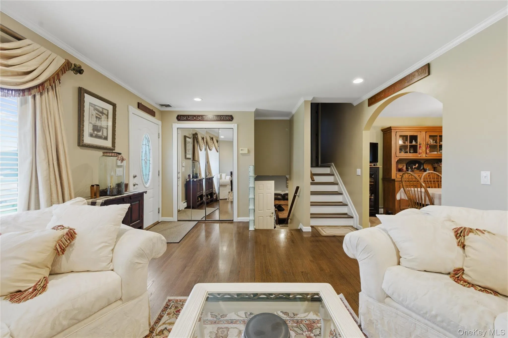 Living room featuring wood-finish flooring, crown molding, an arched entryway, recessed lighting, and a white entry door with decorative glass Living room featuring wood-finish flooring, crown molding, an arched entryway, recessed lighting, and a white entry door with decorative glass