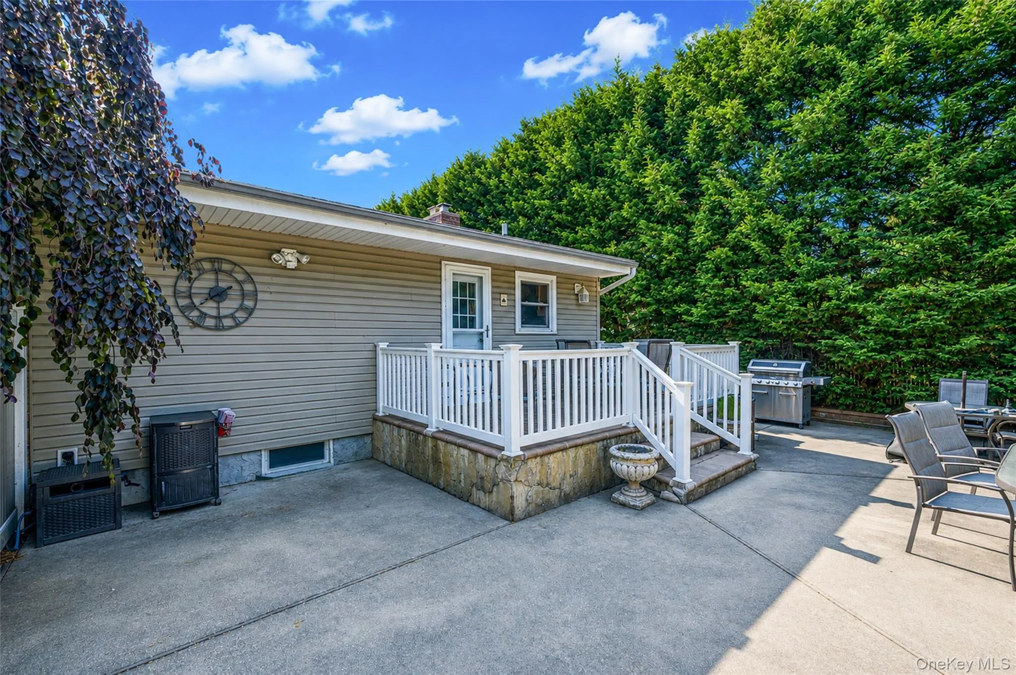 Rear exterior featuring a concrete patio, white railing deck, and mature privacy trees Rear exterior featuring a concrete patio, white railing deck, and mature privacy trees