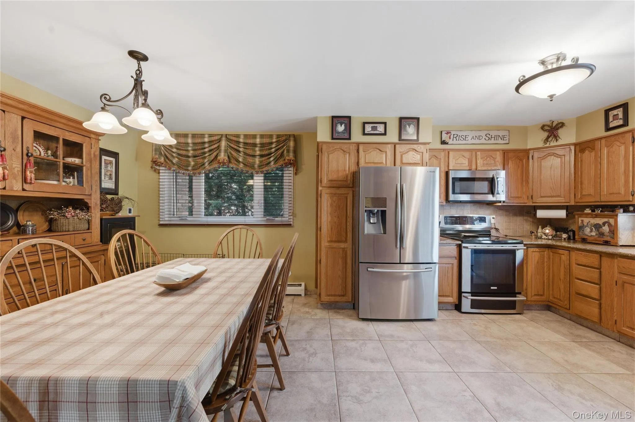 Open-concept kitchen and dining area featuring light wood cabinetry, stainless steel appliances, a built-in hutch, and tiled flooring Open-concept kitchen and dining area featuring light wood cabinetry, stainless steel appliances, a built-in hutch, and tiled flooring